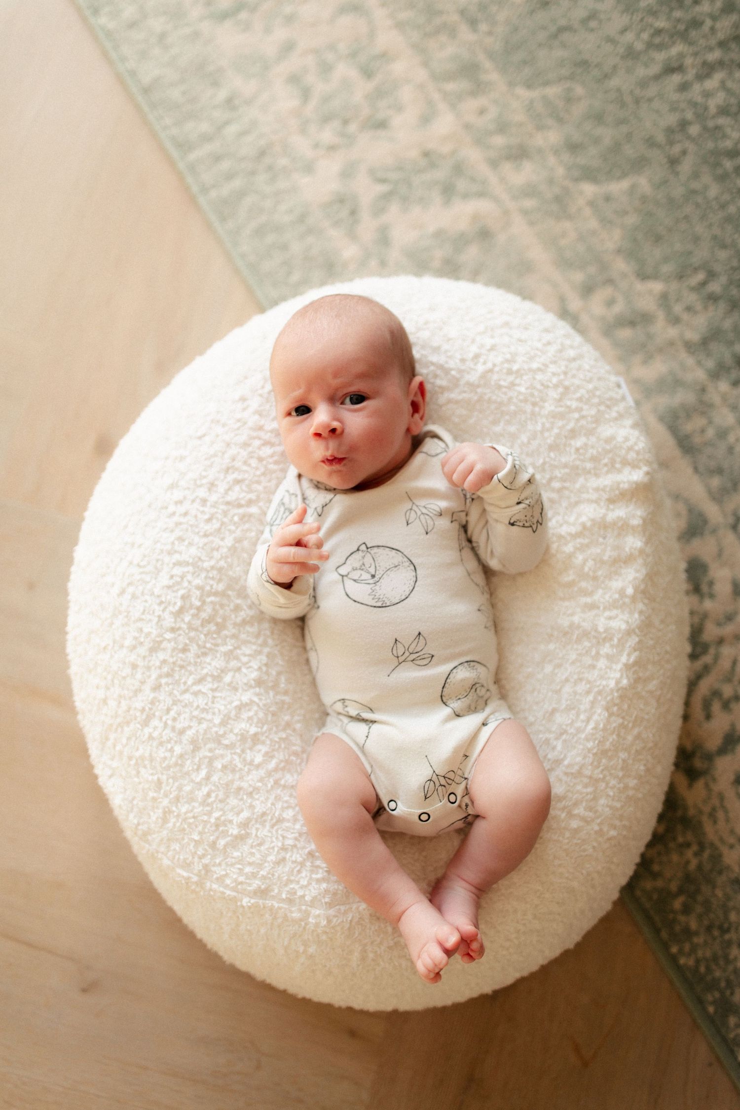 Infant in a patterned onesie resting on a plush white circular pillow.