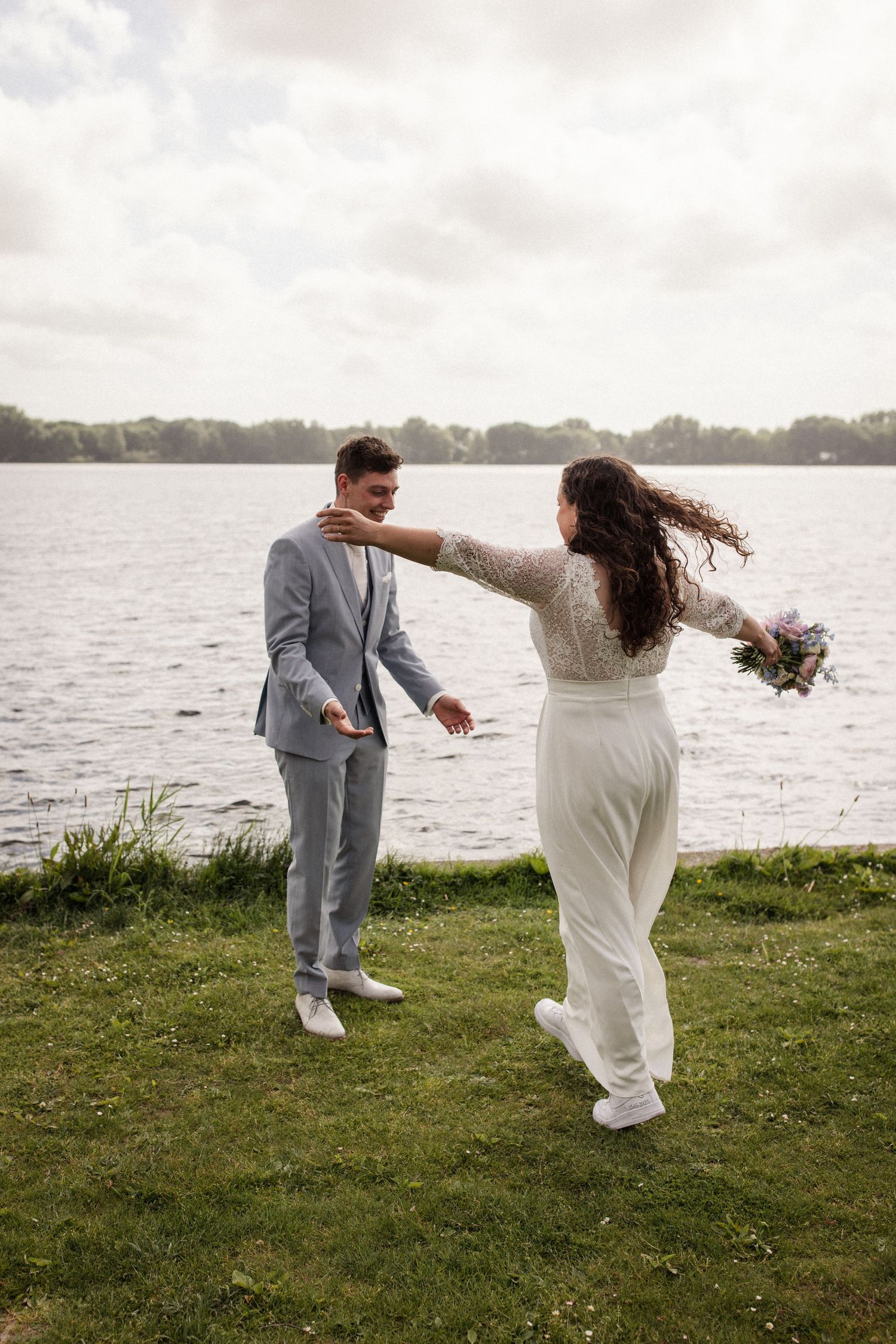 Playful wedding couple dancing by the waterfront on a grassy lawn.
