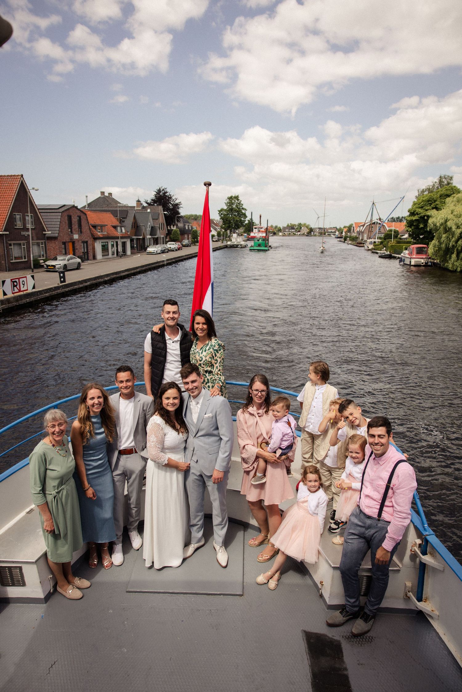 Wedding party members gather on a boat deck with waterfront houses visible in the background.