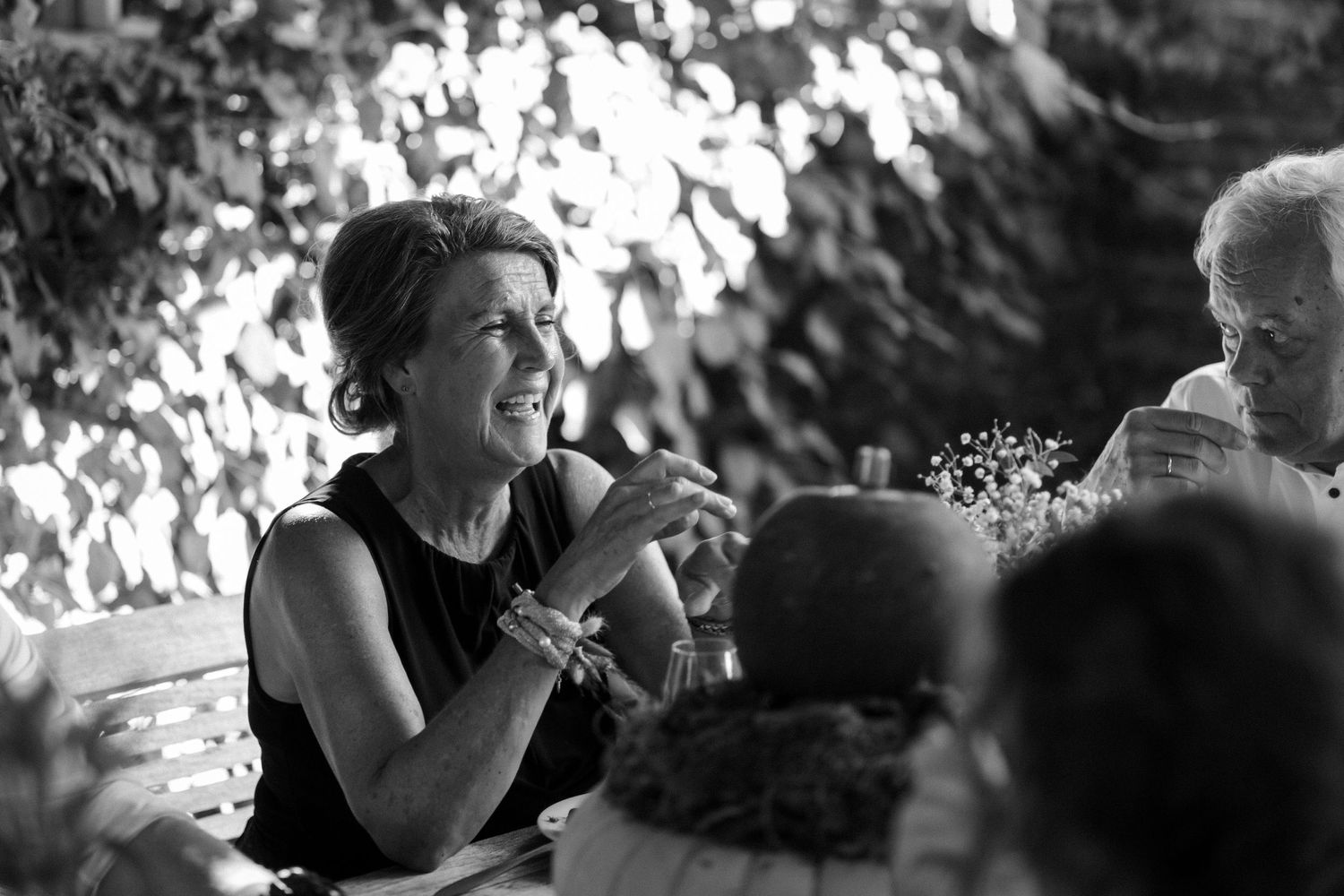 A candid black and white photograph captures someone laughing during an outdoor gathering with others.