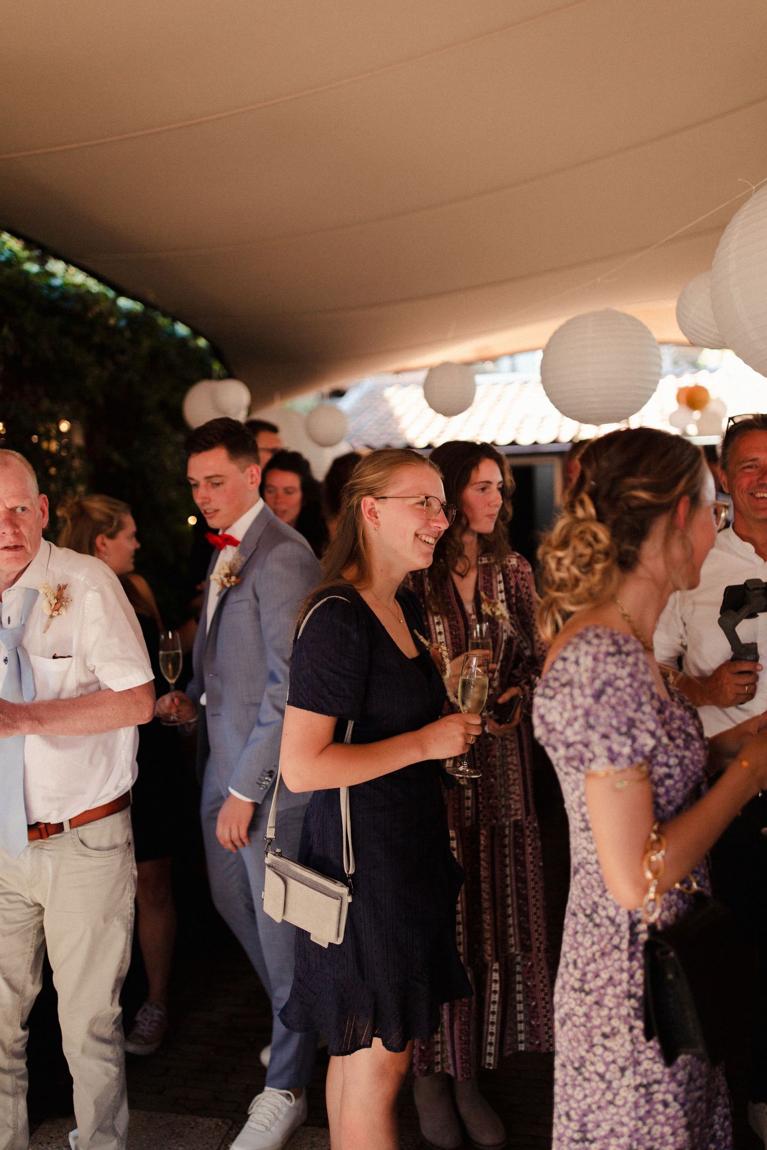Wedding guests gather under white paper lanterns at an evening reception celebration.