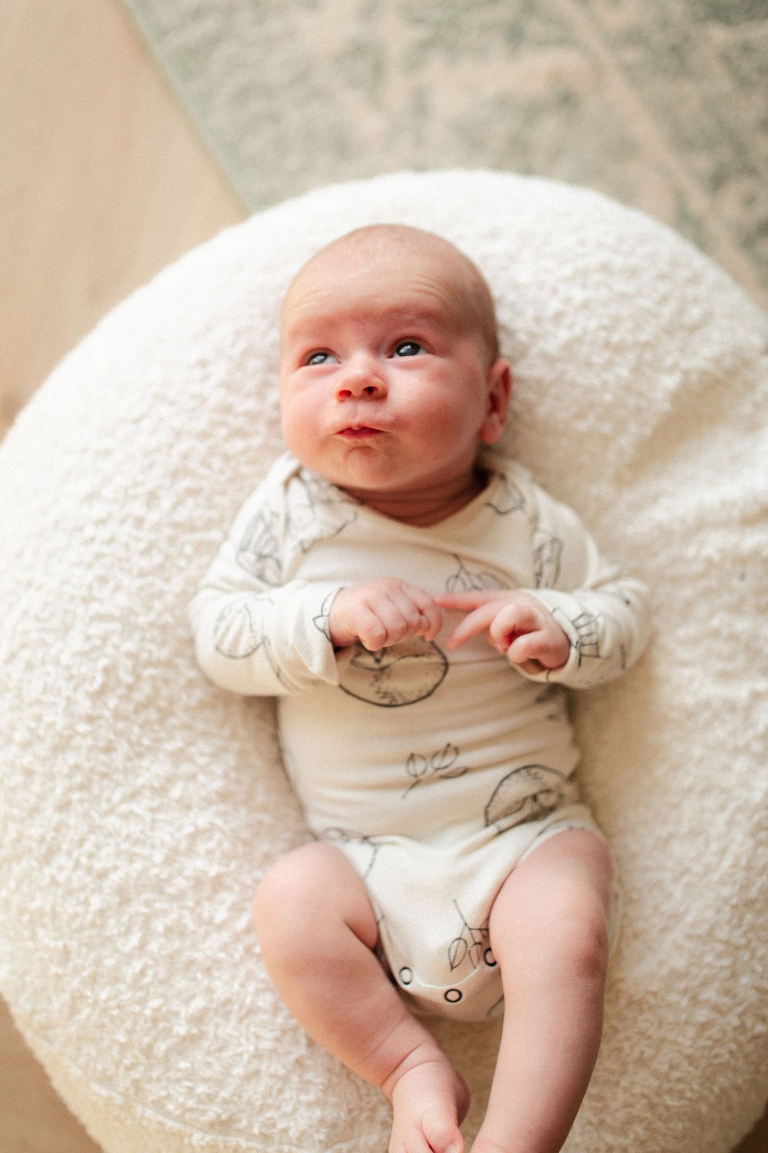 Baby in an illustrated onesie lying on a round white cushion.
