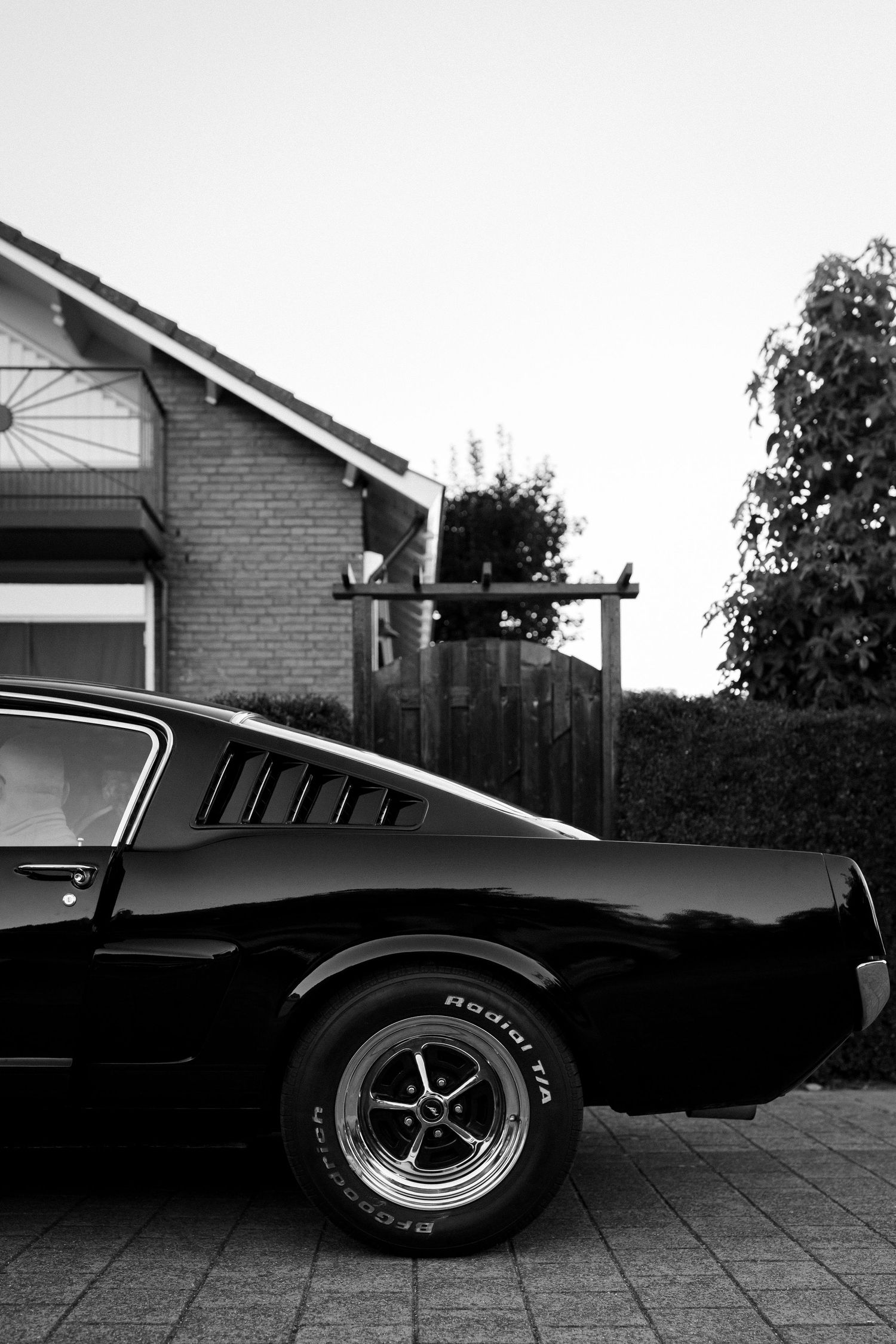 Classic black Ford Mustang fastback with chrome wheel showing rear quarter panel and signature C-pillar louvers.