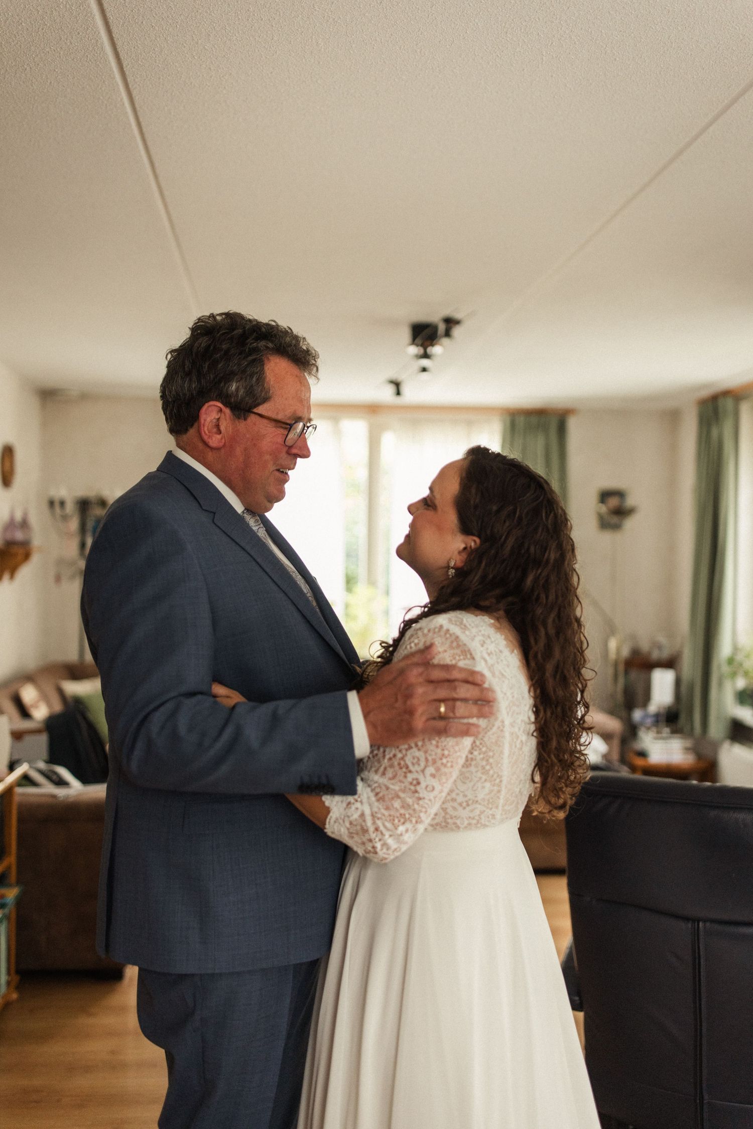 Tender moment between bride in lace dress and person in suit during wedding preparations.