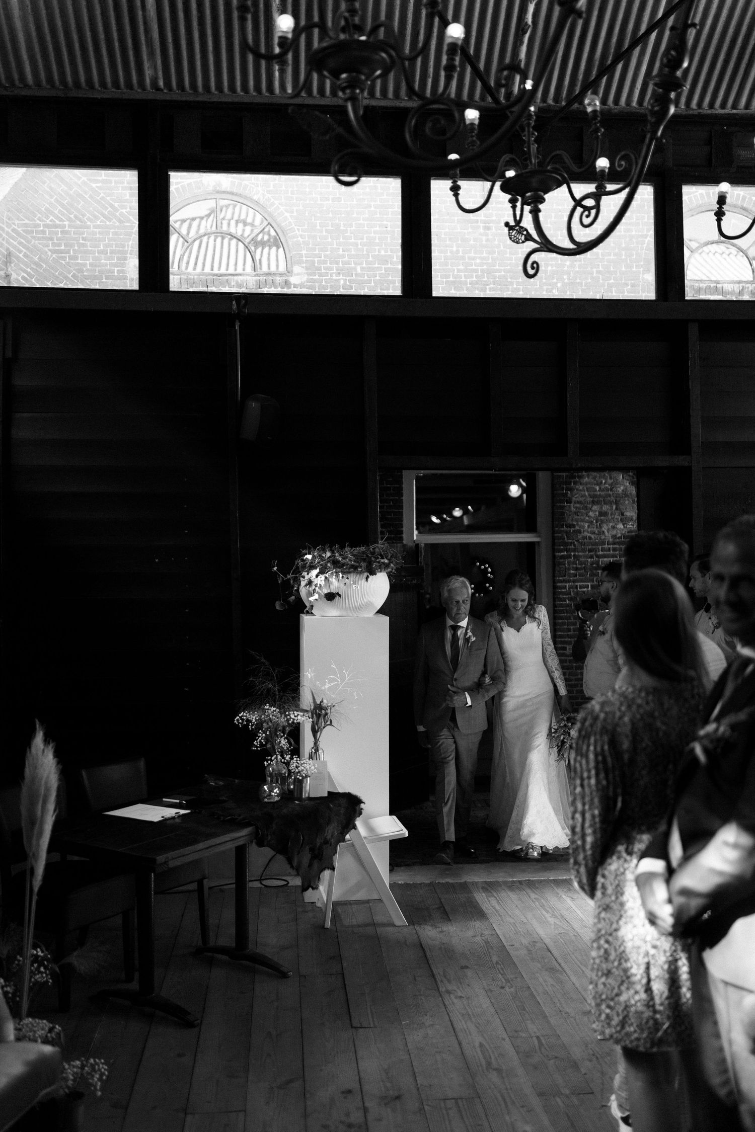 Black and white photo of a wedding reception in a rustic venue with chandeliers and wooden floors.
