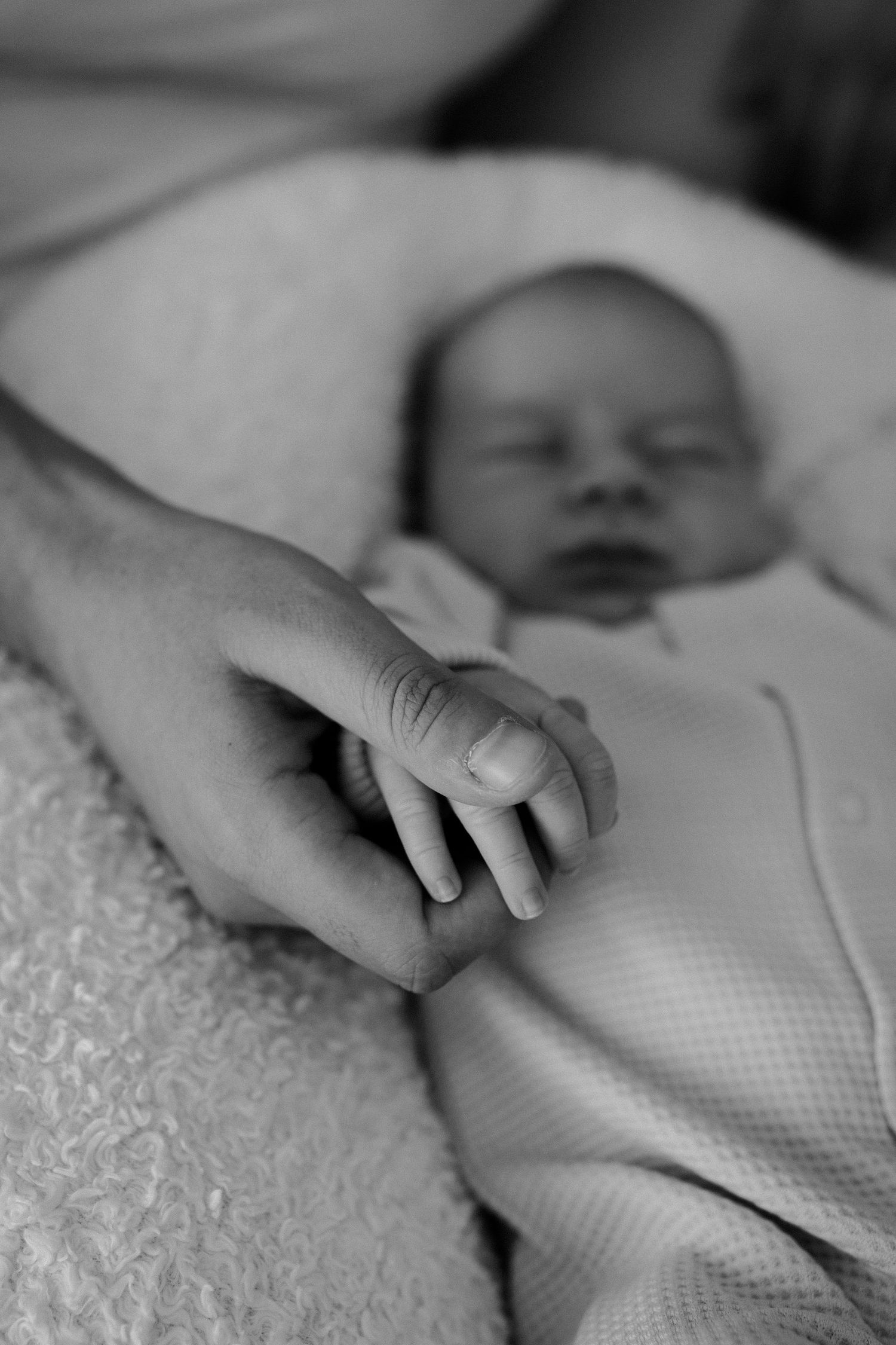Black and white closeup of newborn baby's hand being held.