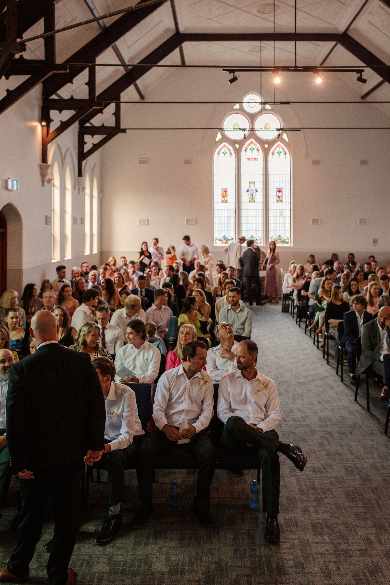 Wedding ceremony in a church with high ceilings and stained glass windows filled with guests.