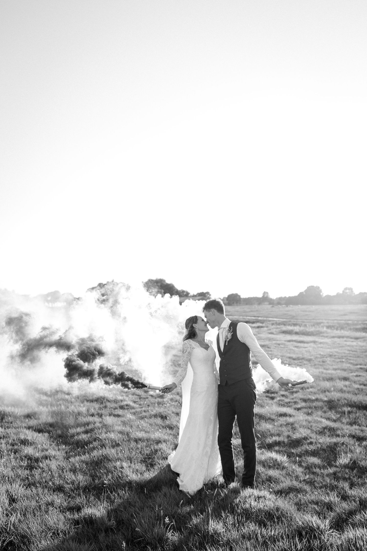 Romantic black and white wedding photo with smoke effects in a field at golden hour.