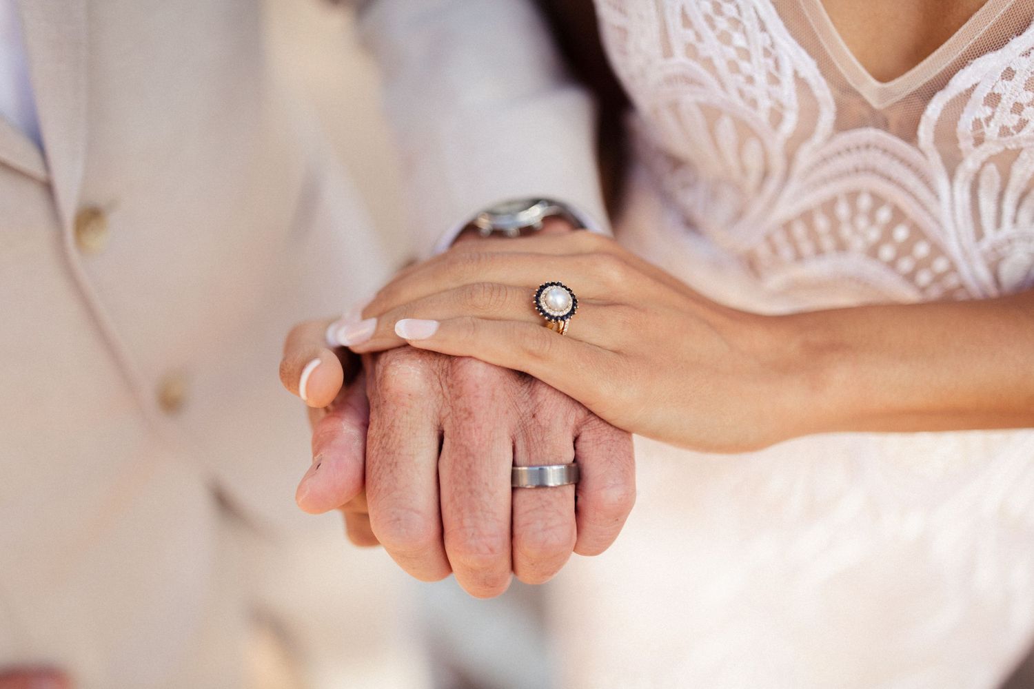 Close-up of newlywed hands with wedding rings showing delicate lace dress details.