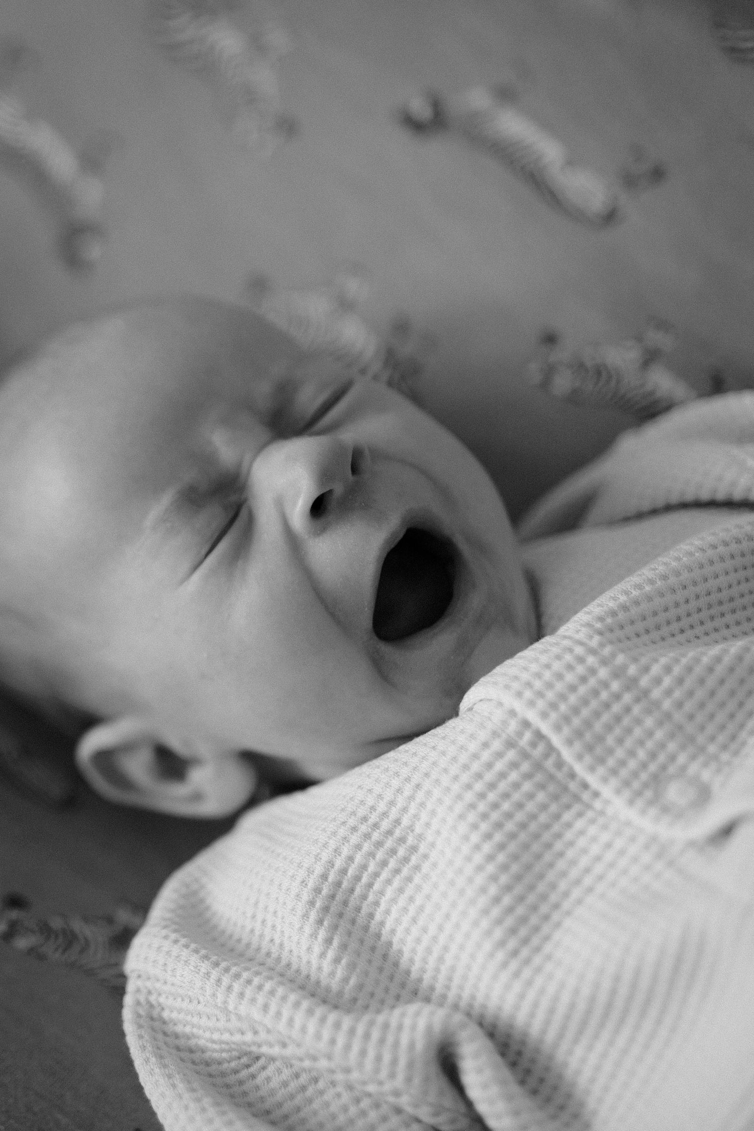 A black and white photo of a baby yawning while lying down.