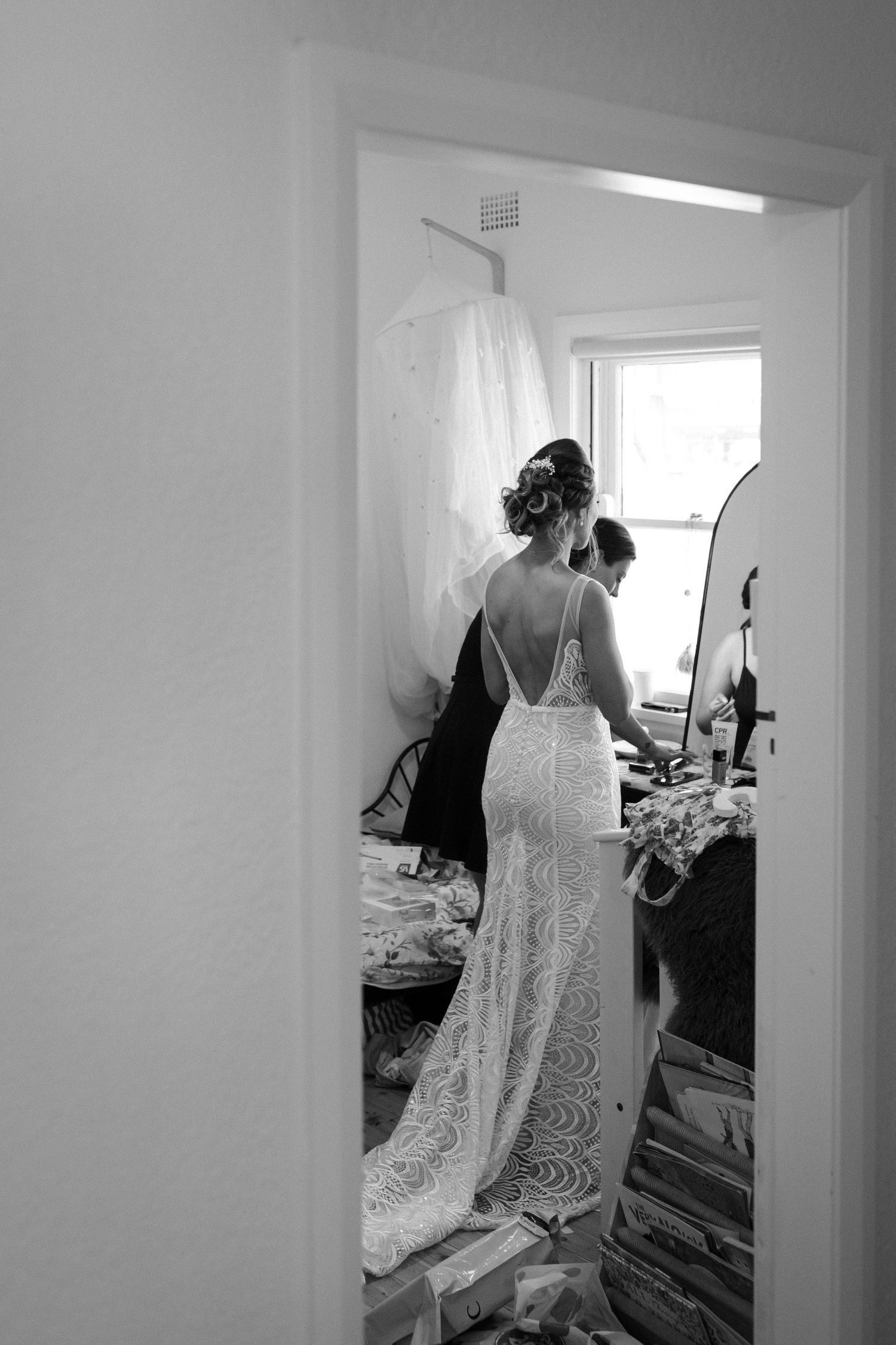 Back view of a lace wedding dress being fitted in a sunlit room.