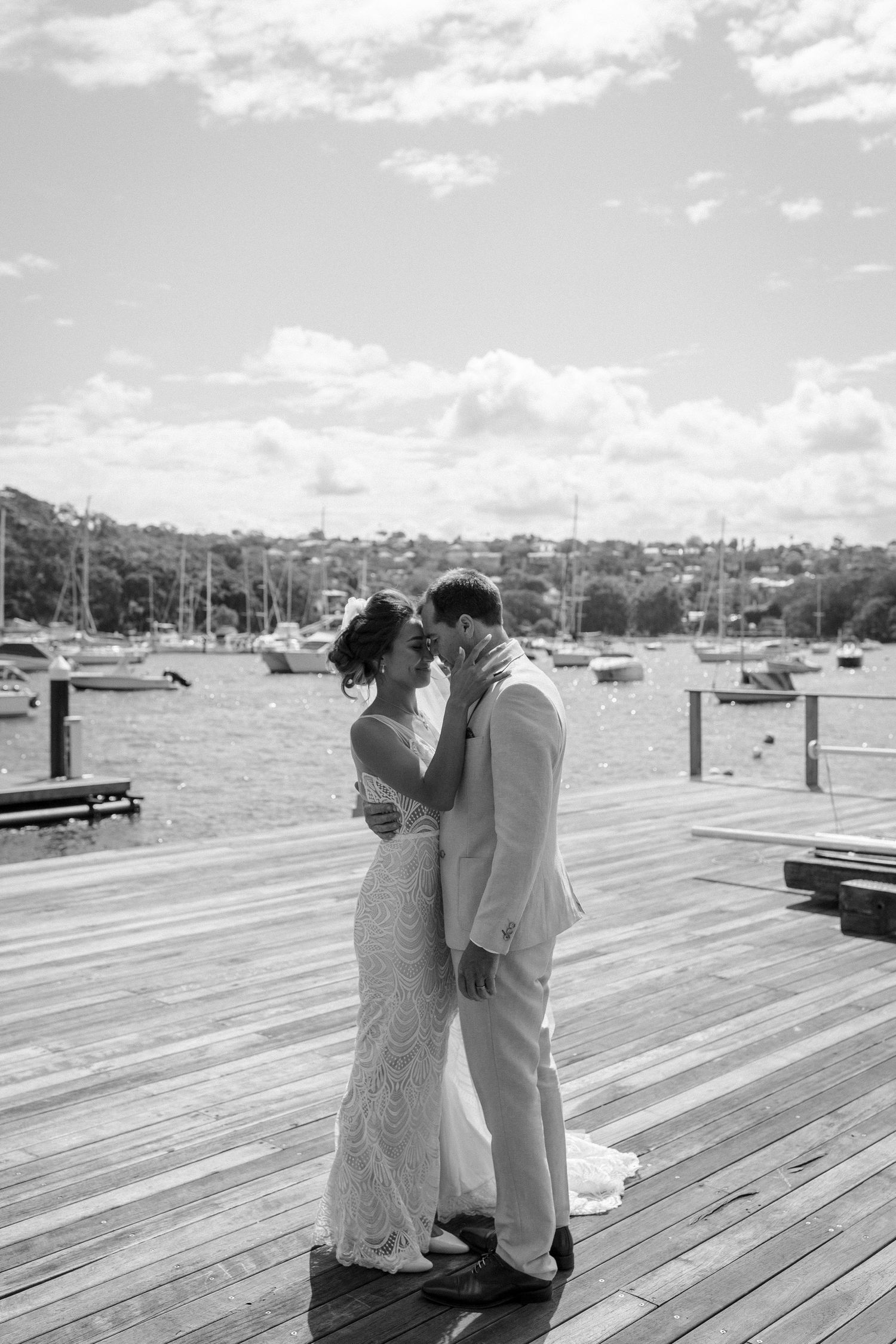 Black and white portrait of couple in wedding attire on harbor dock.