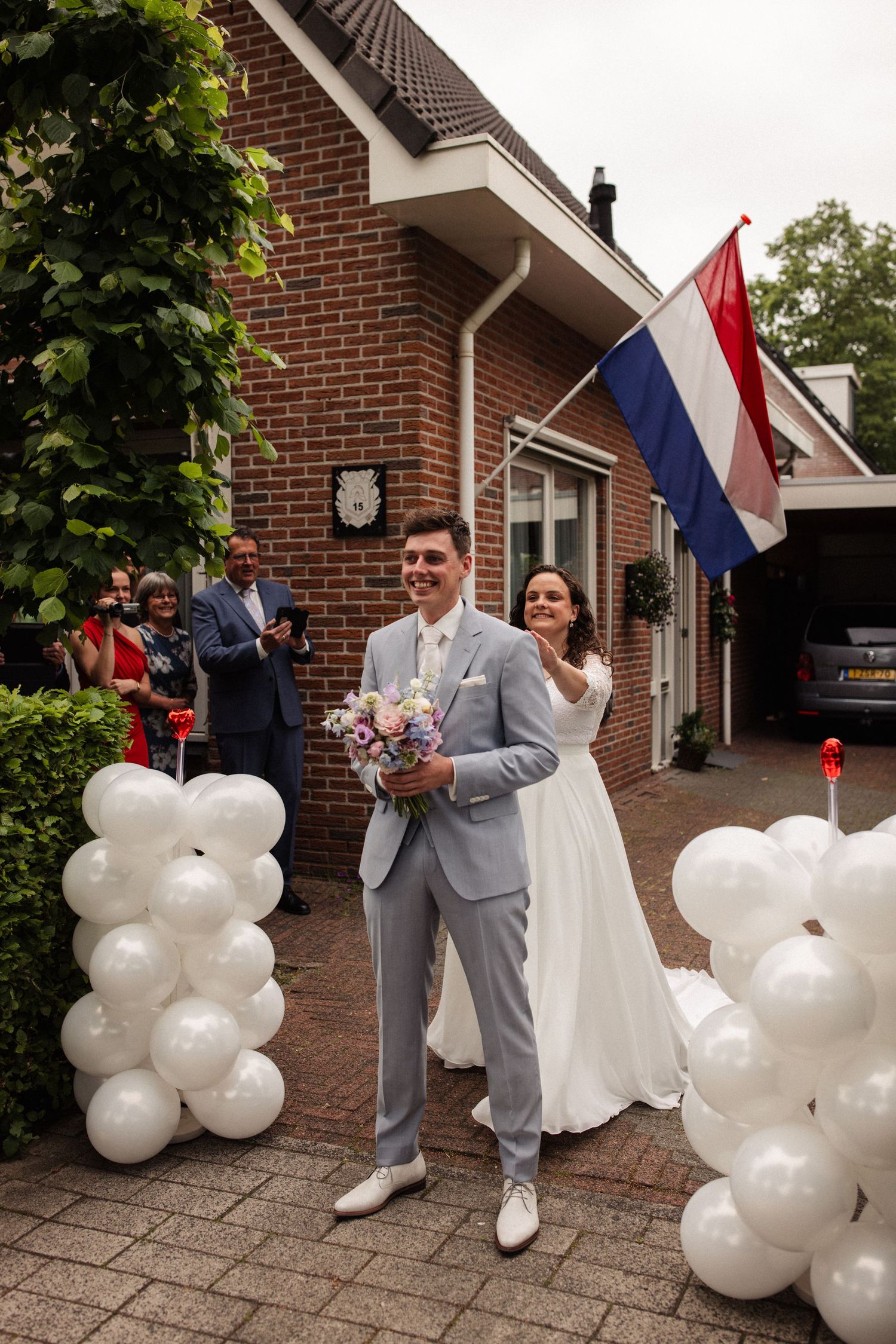 Wedding celebration outside brick house with white balloons and Dutch flag decorations.