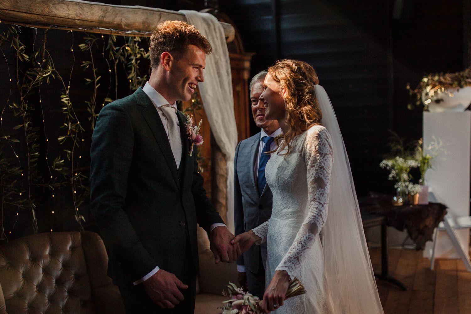 A couple shares a joyful moment together during their intimate indoor wedding ceremony beneath decorative lights.