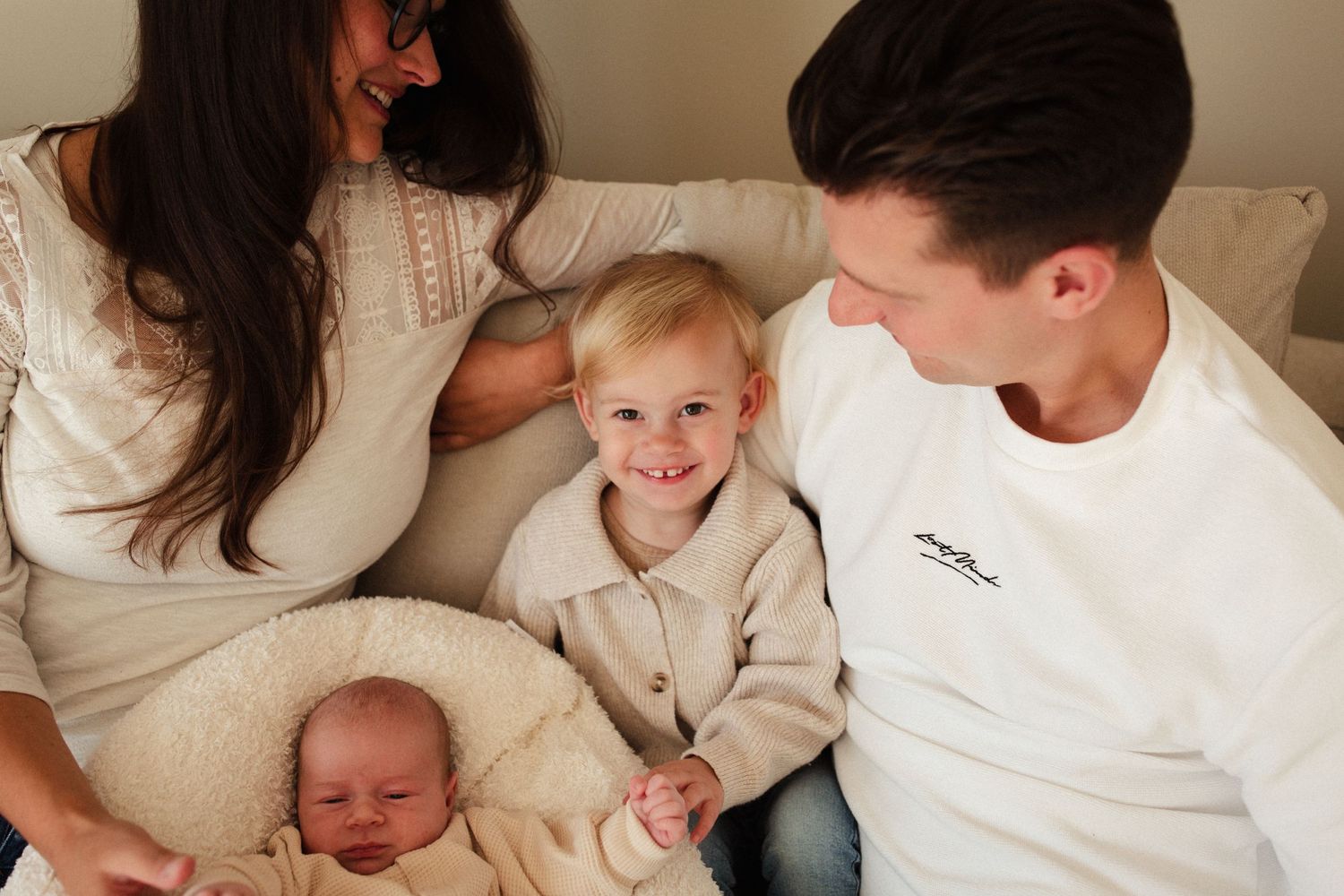 Family portrait showing tender moment with toddler and newborn on couch.
