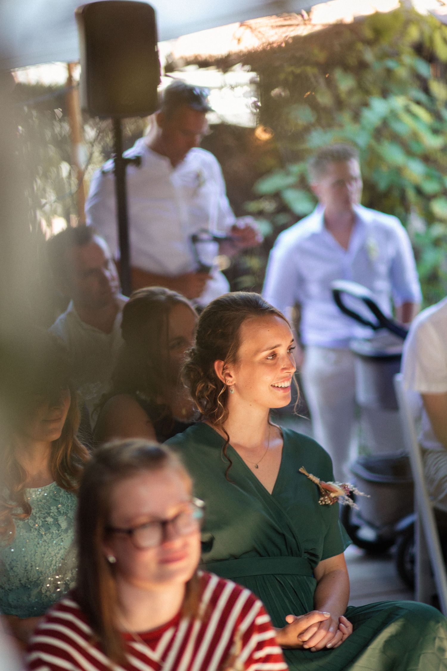 People gathered outdoors at a social event with lush greenery visible in the background on a sunny day.