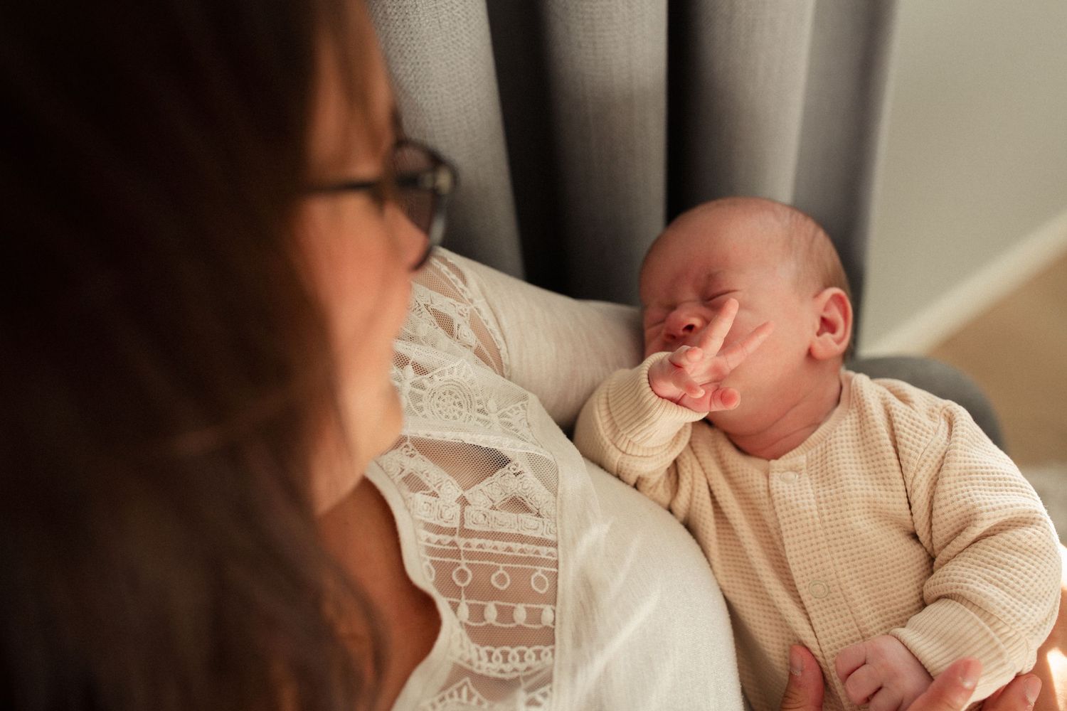 Closeup of a baby yawning in beige clothing while being held.