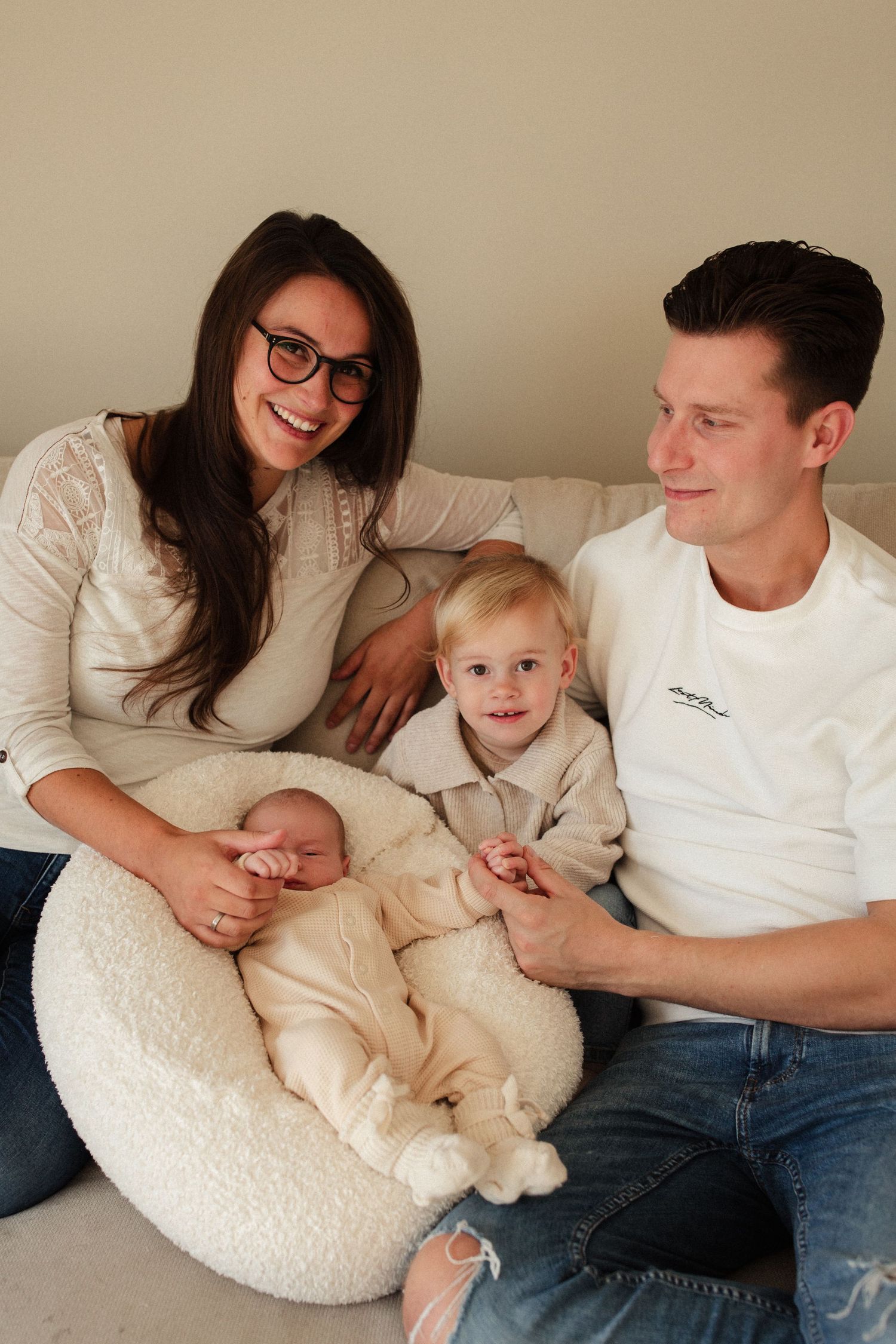 Family of four sitting together on white couch in coordinated cream and white outfits.