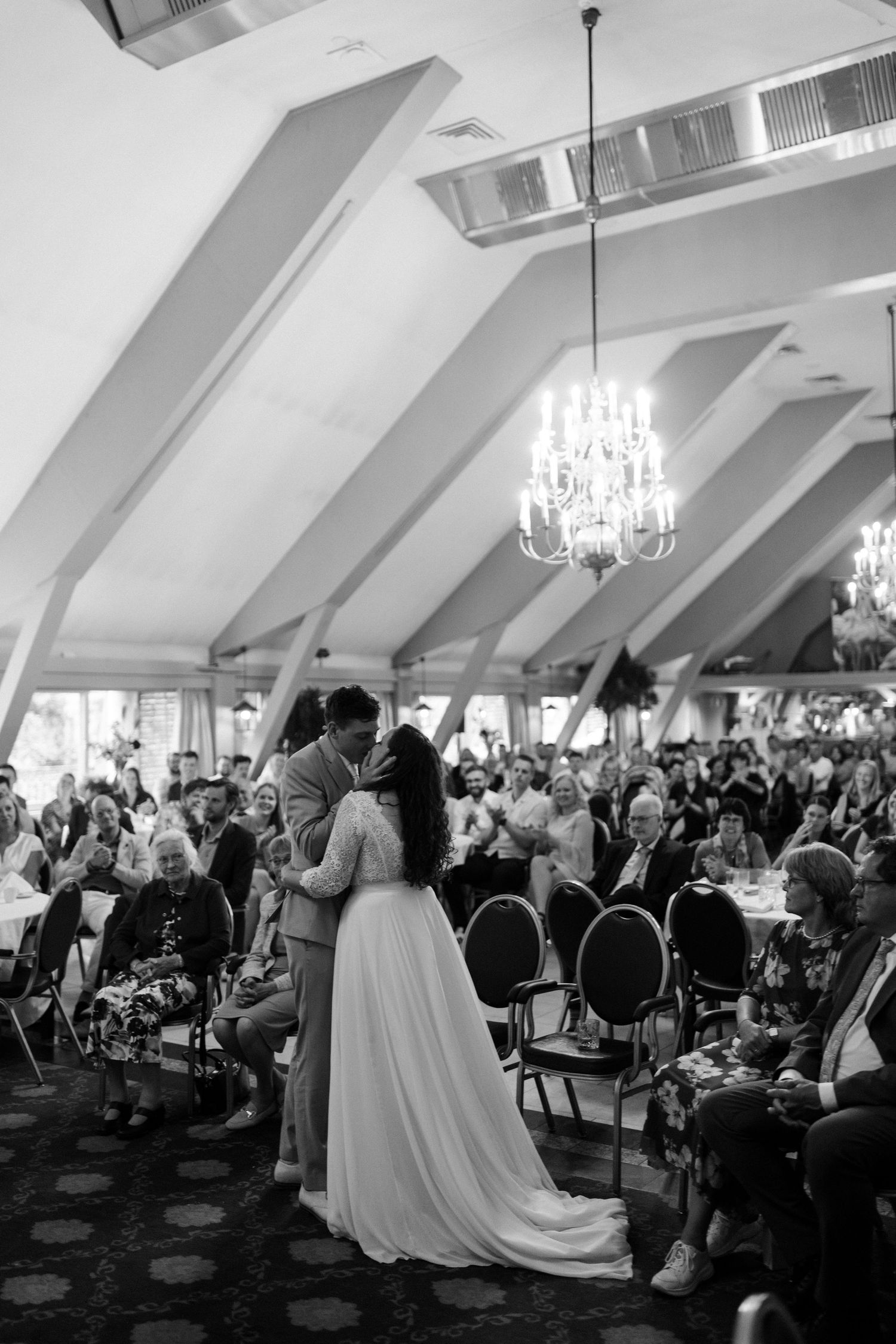 Black and white wedding reception photos show a bride in a white gown approaching the dance floor under elegant chandeliers.