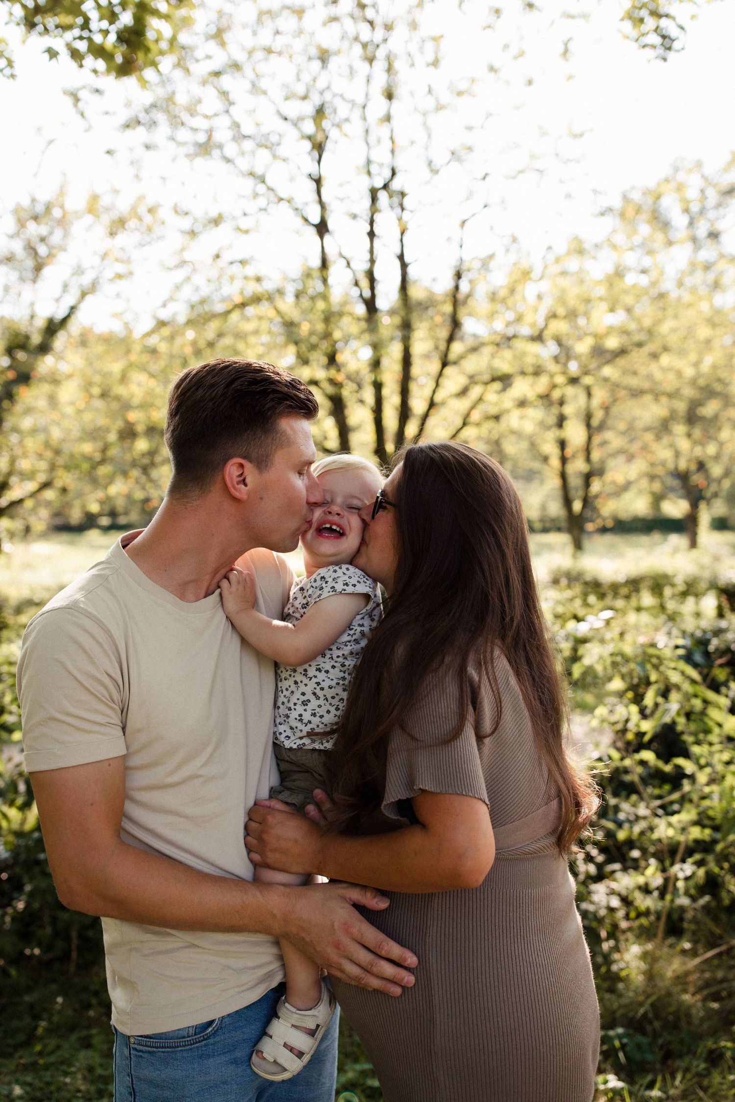 Tender family moment captured in a sunlit garden setting on a warm day.