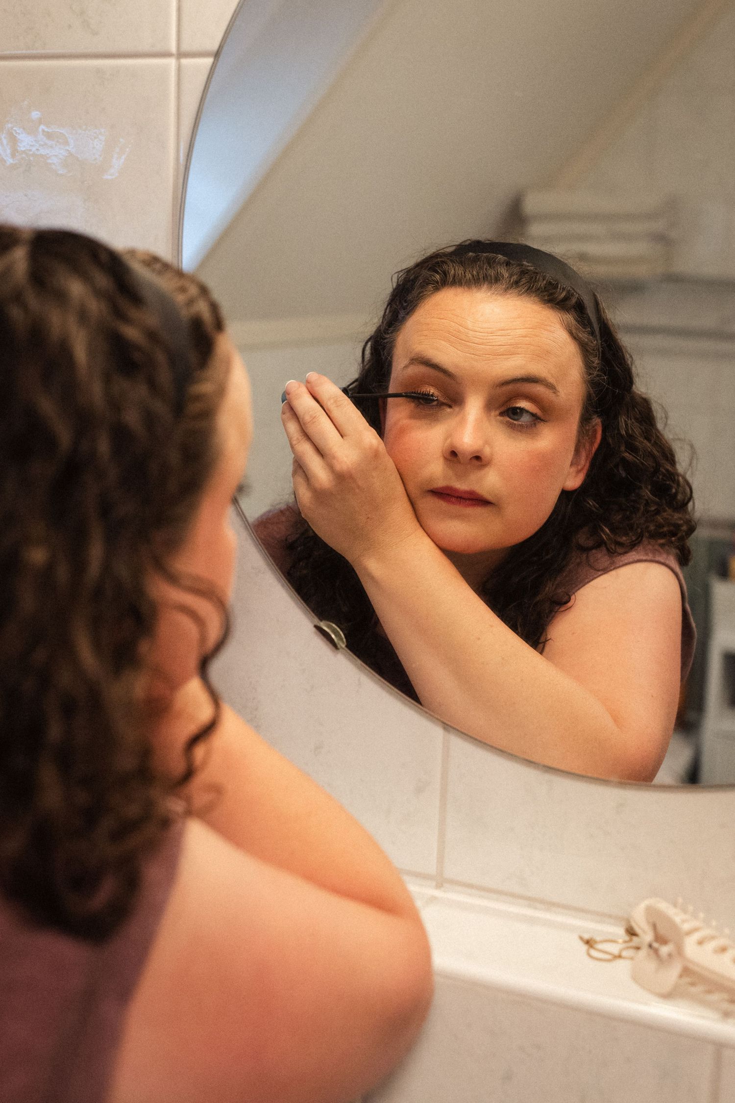Person applying makeup while looking in bathroom mirror during wedding preparations.