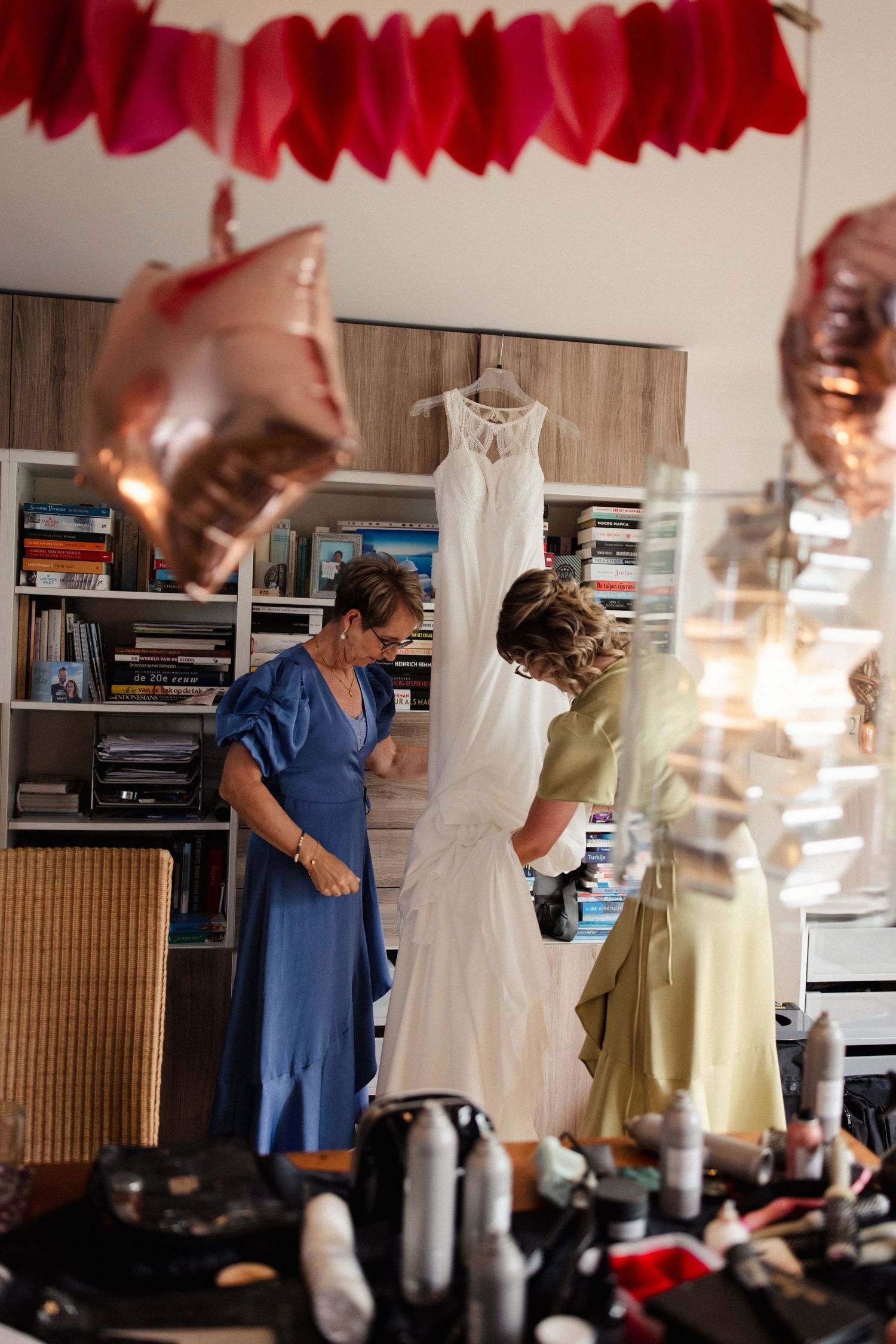 Wedding dress preparations in a room decorated with red paper garlands and hanging gowns.