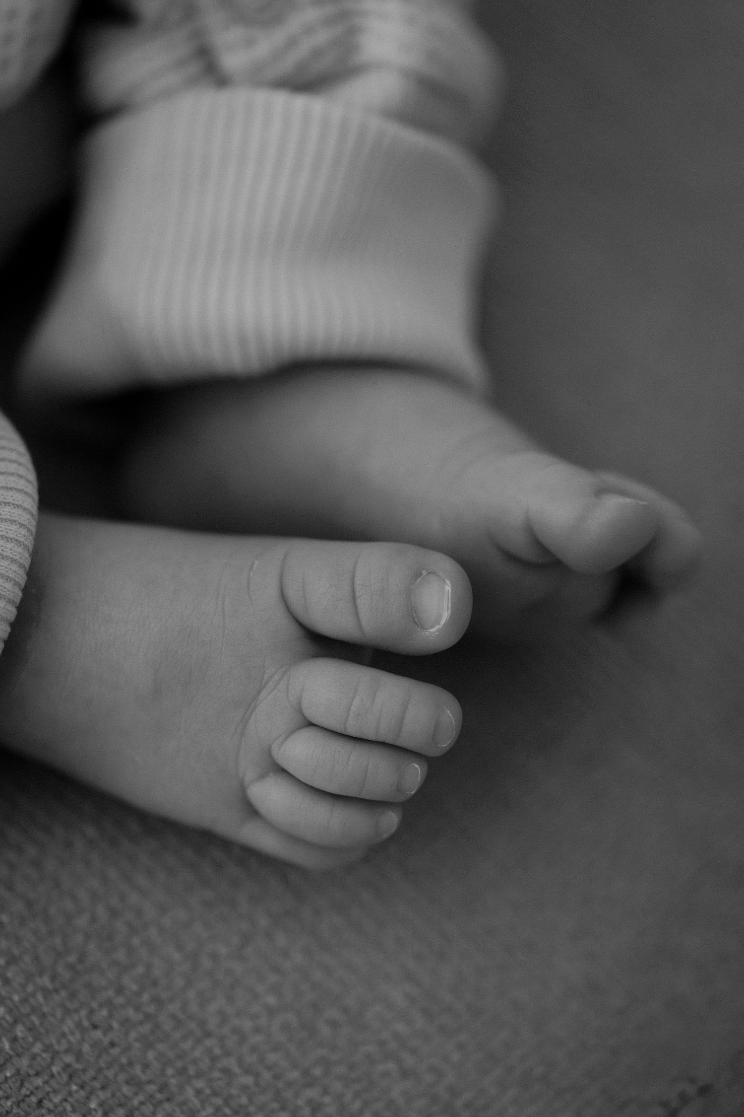 Close-up black and white photo of tiny baby toes and feet against a textured background.