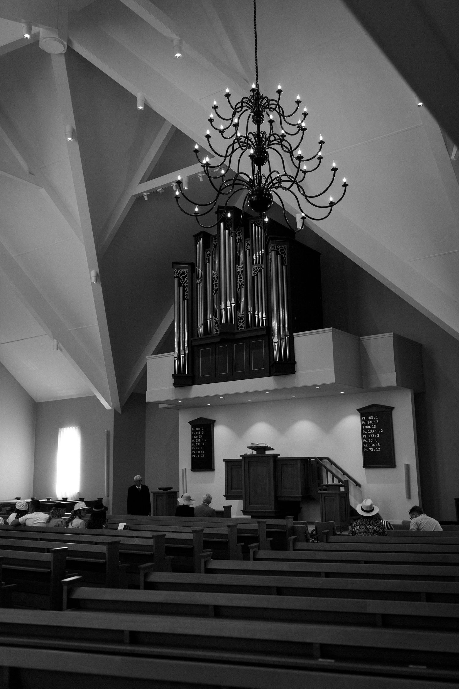 Black and white photograph of a church interior with wooden pews and a grand pipe organ mounted high on the wall.