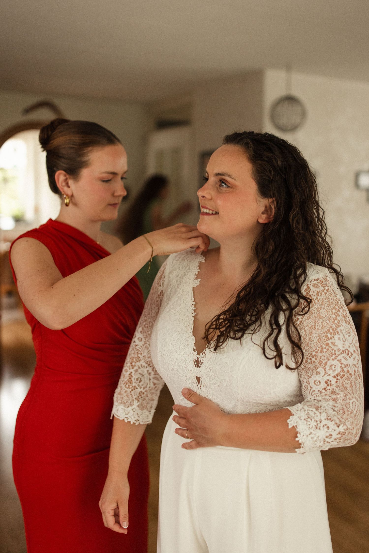 Two people embrace and share joyful moments in a wedding setting with one wearing a white lace dress and another in red.