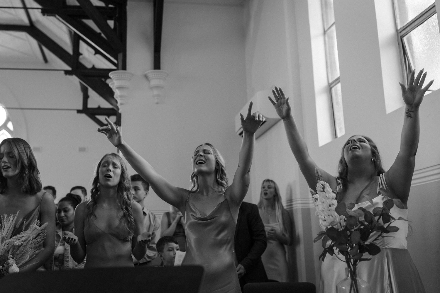 Black and white photo of joyful wedding celebration with raised hands in a church.