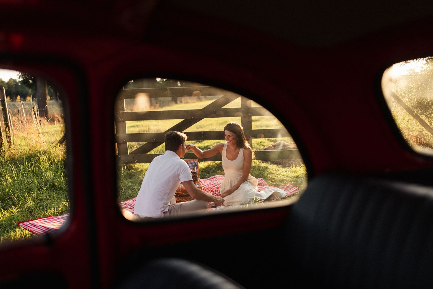 Koppel die zit te picknicken in de natuur, geframed door de achterruit van een klassieke fiat.