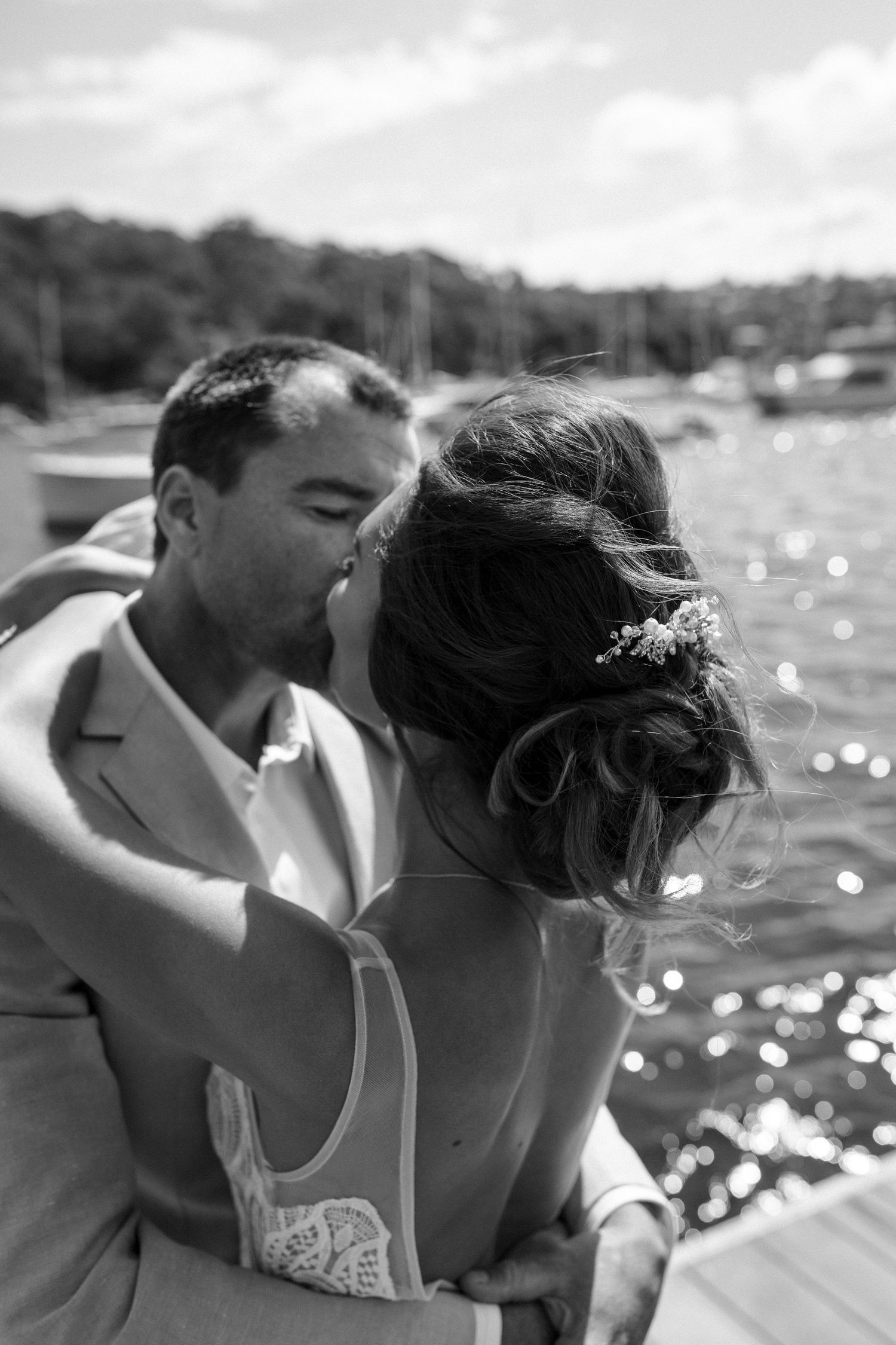 A black and white wedding photo showing a romantic embrace on a waterfront dock.