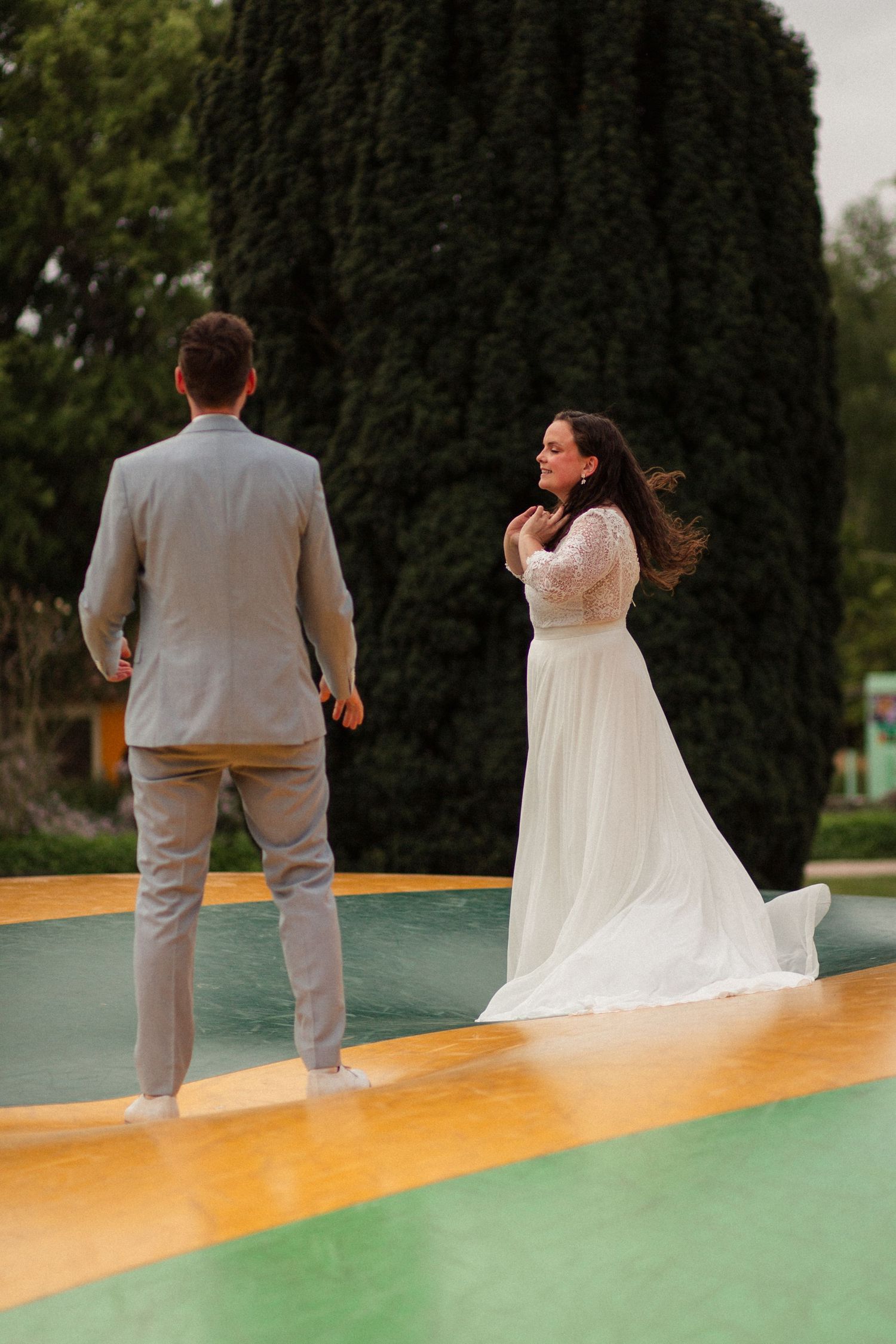 Couple on a colorful outdoor platform sharing a playful moment in wedding attire.