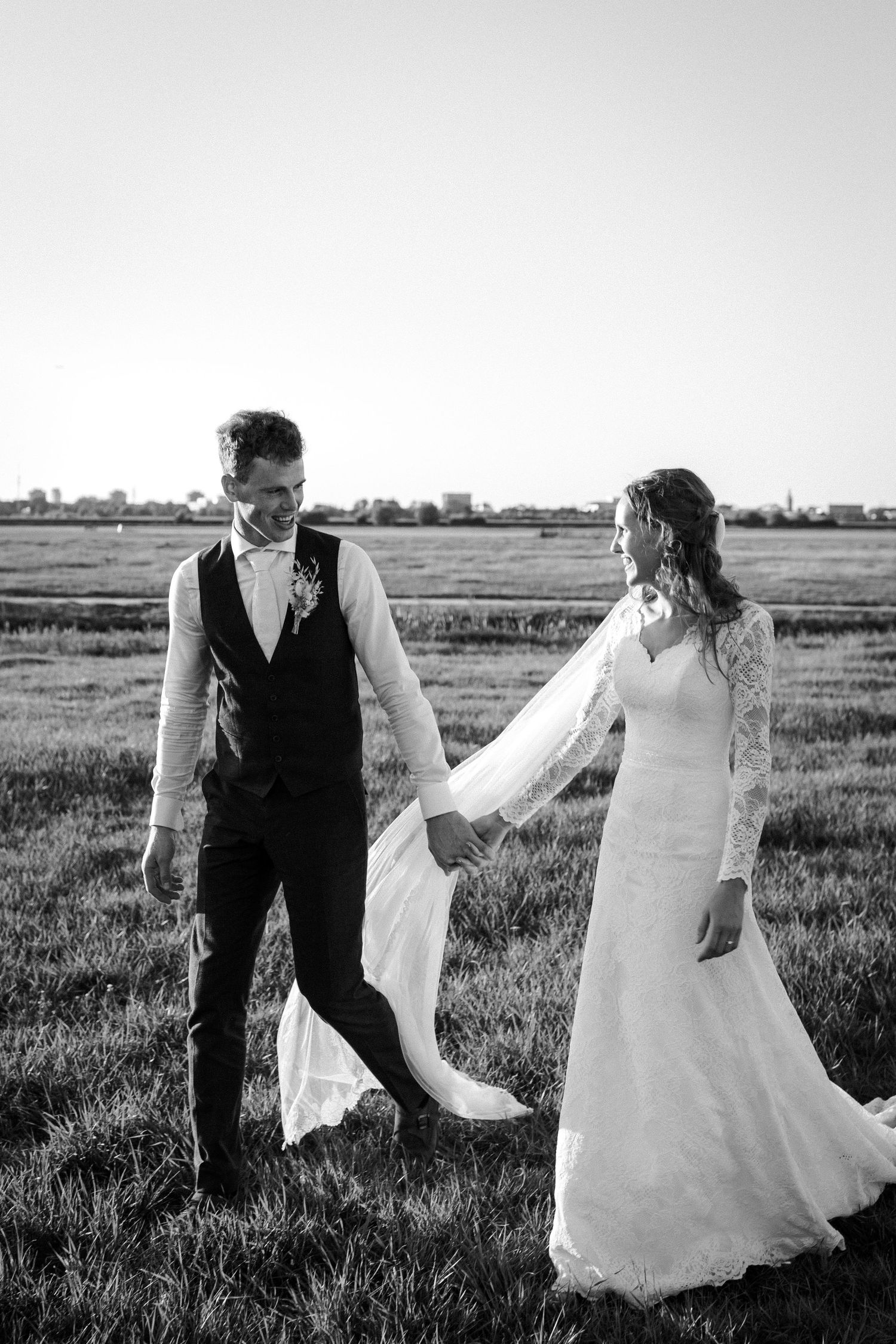 A black and white wedding photo showing a couple holding hands in a grassy field on their special day.