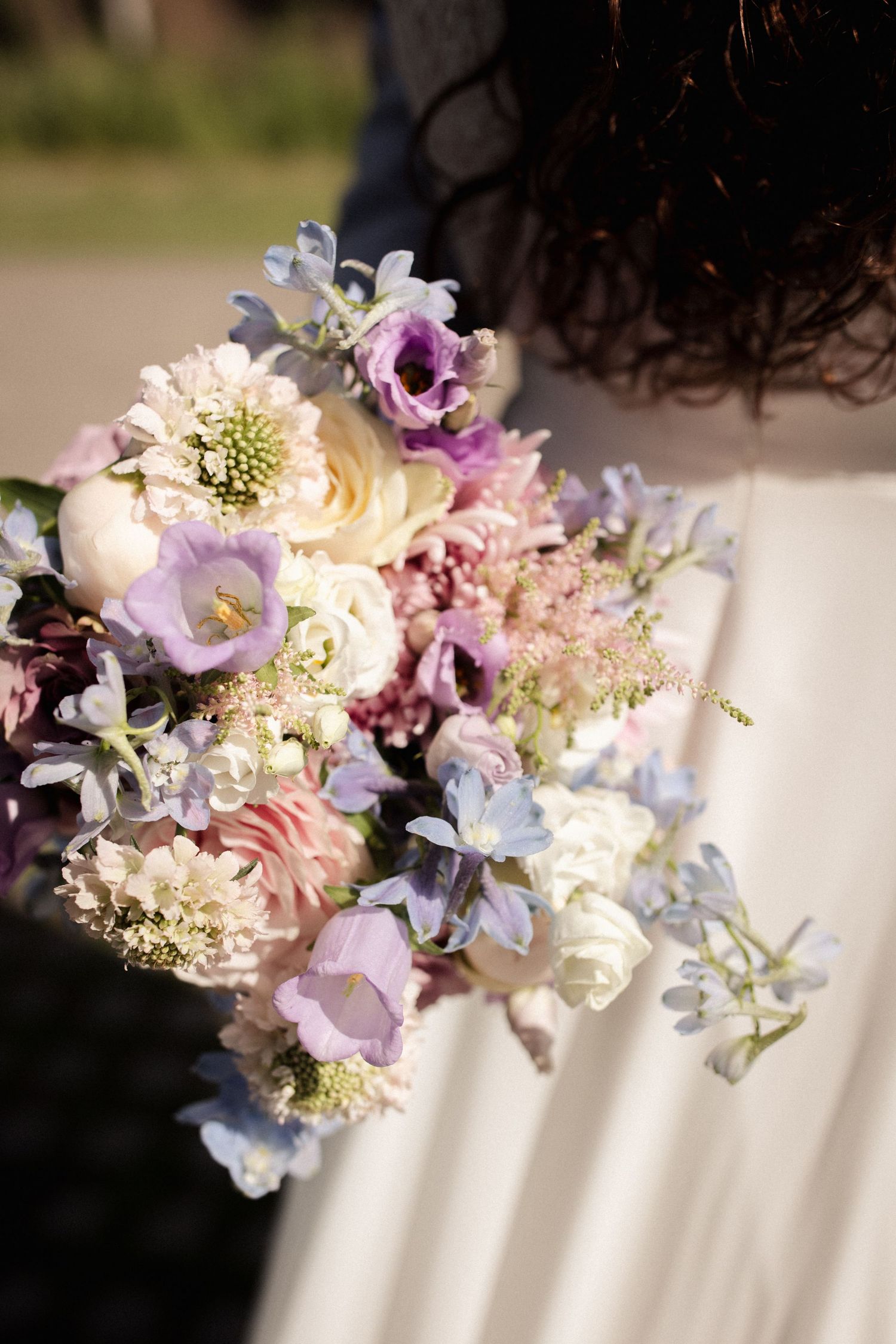 Delicate floral arrangement featuring purple, pink and white blooms with soft textures against a white background.