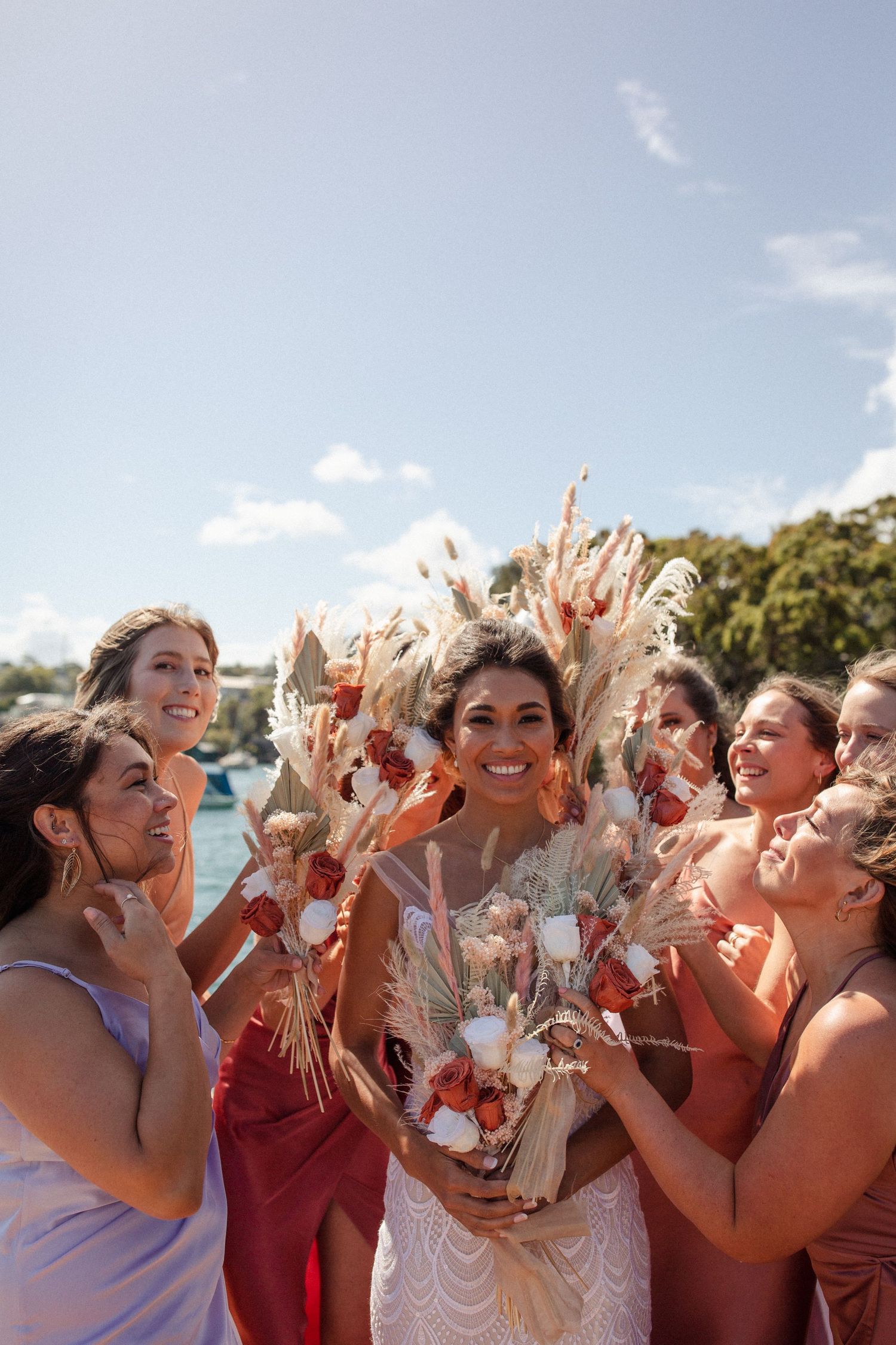 A celebration with bridesmaids in coral dresses cheering around a bride holding dried flowers.
