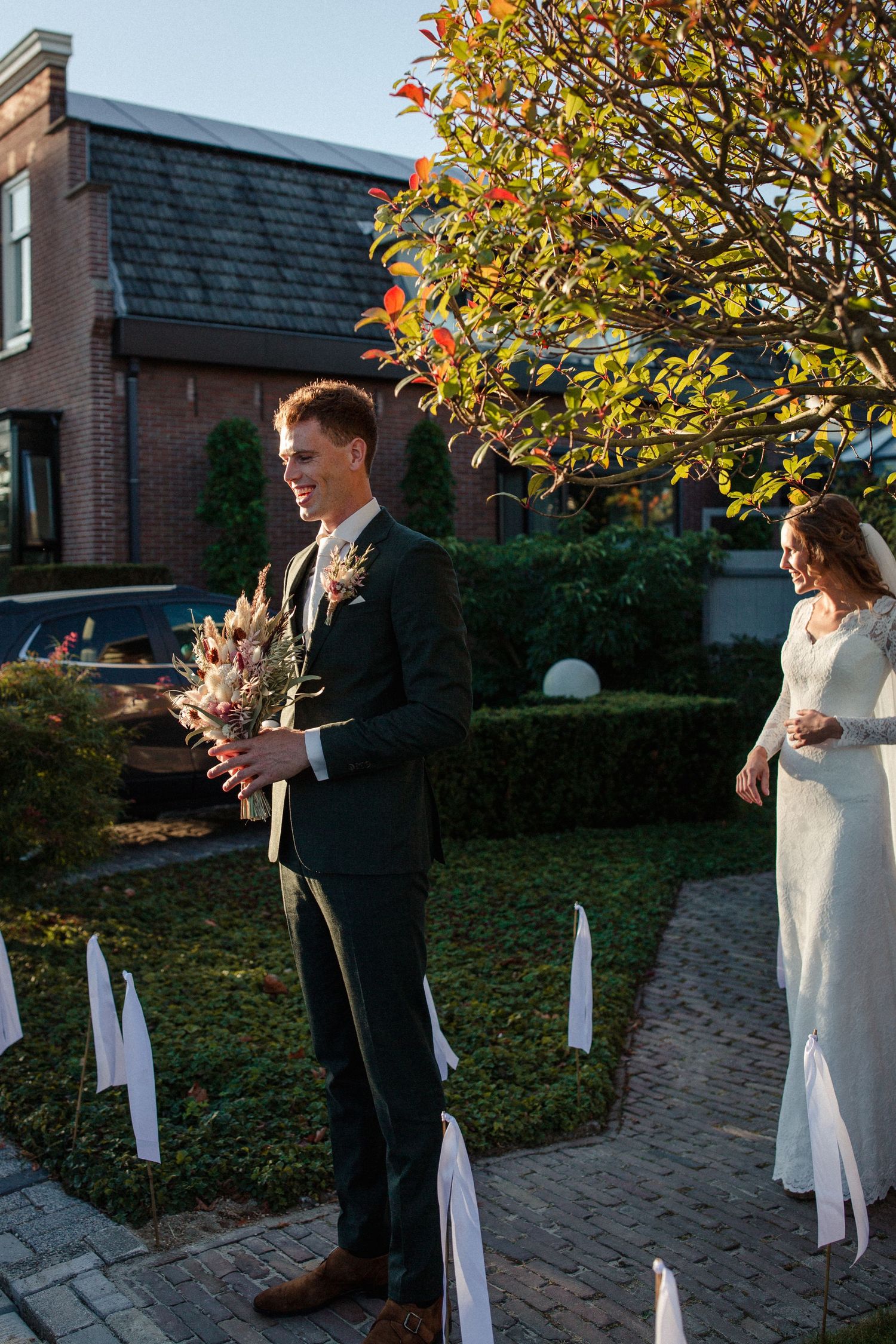An outdoor autumn wedding ceremony setup with a brick house backdrop and colorful fall foliage.
