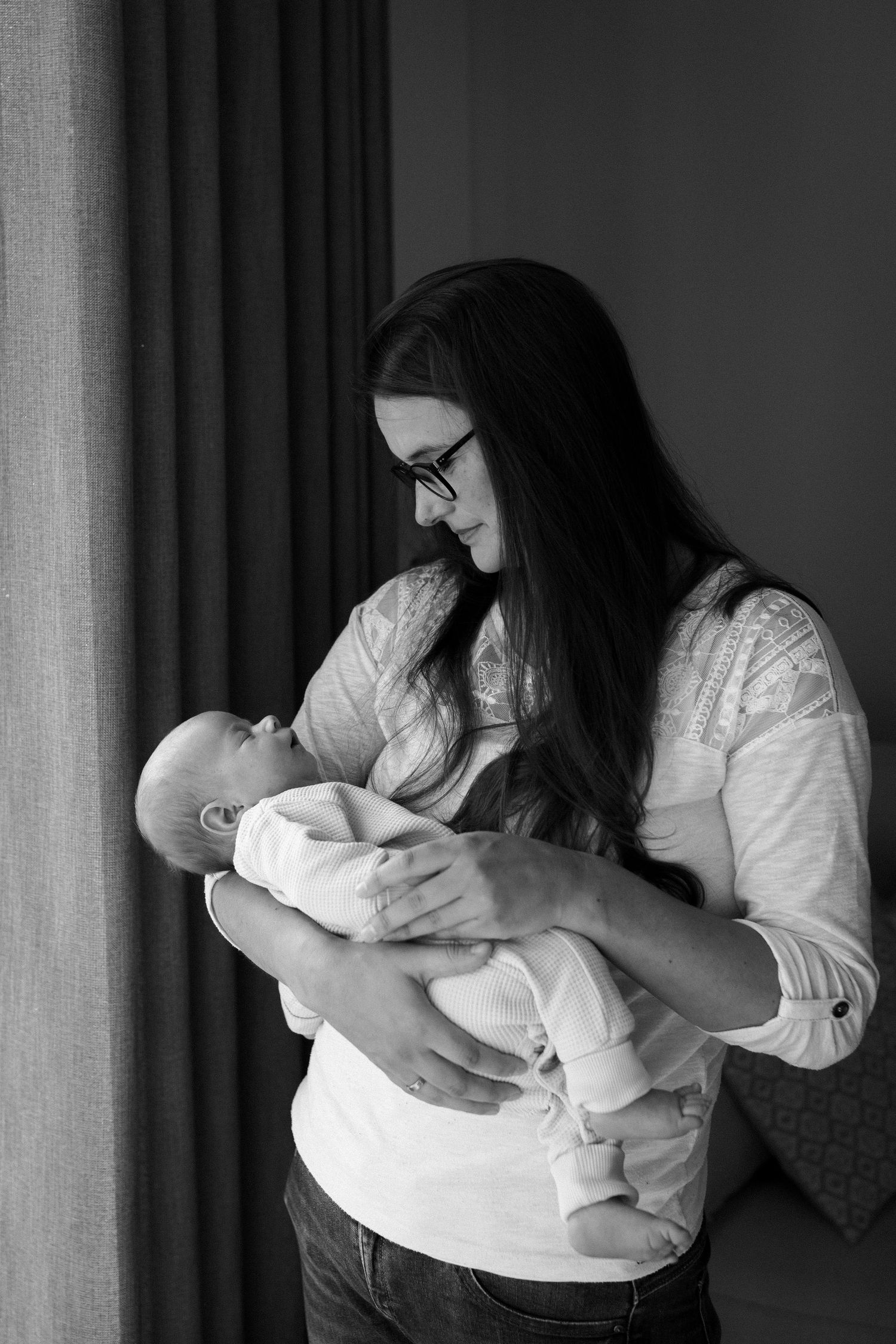 Woman with long dark hair cradling baby in white room.