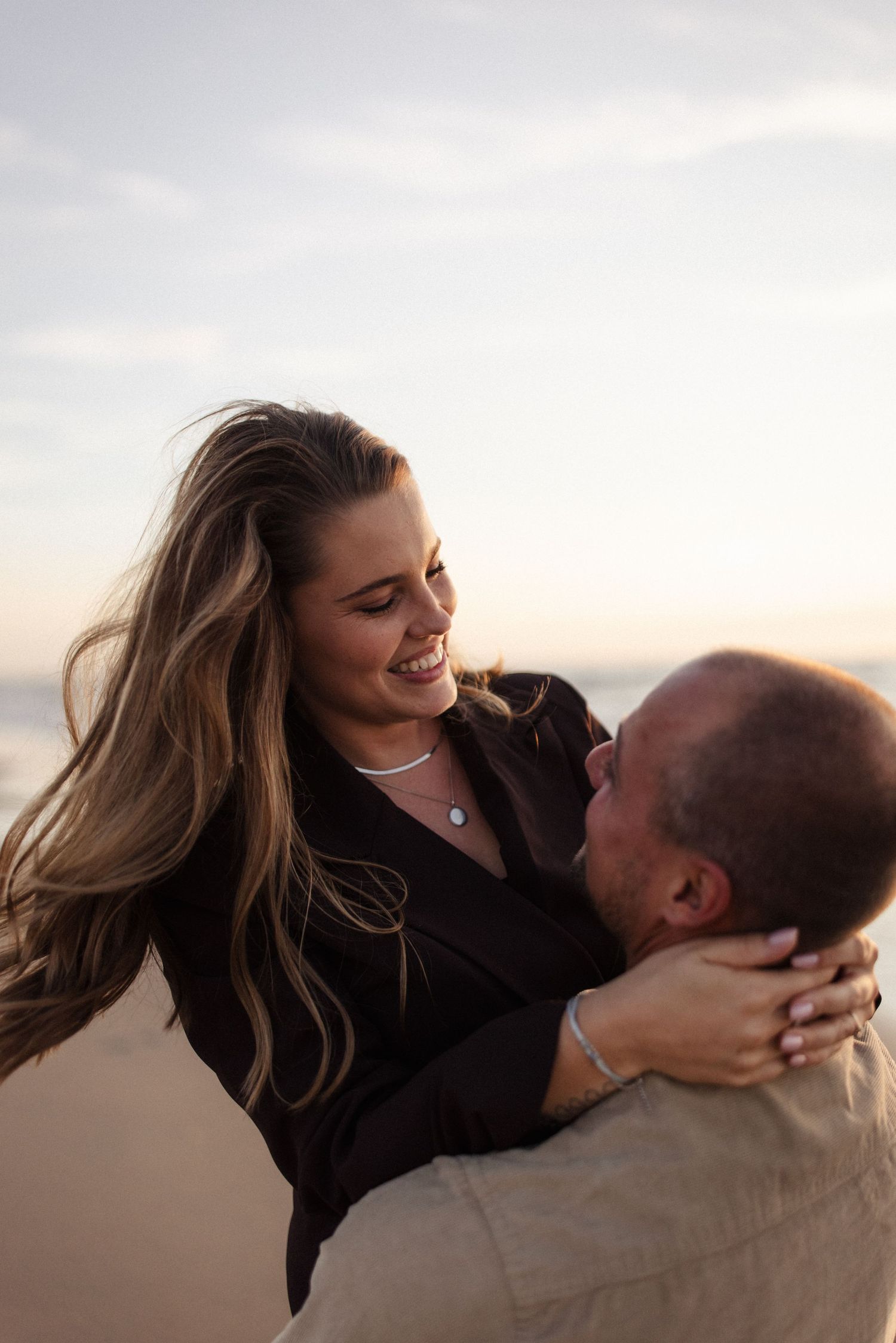 Vrouw die wordt opgetild en rondgedraaid door haar man. Scene is op het strand.