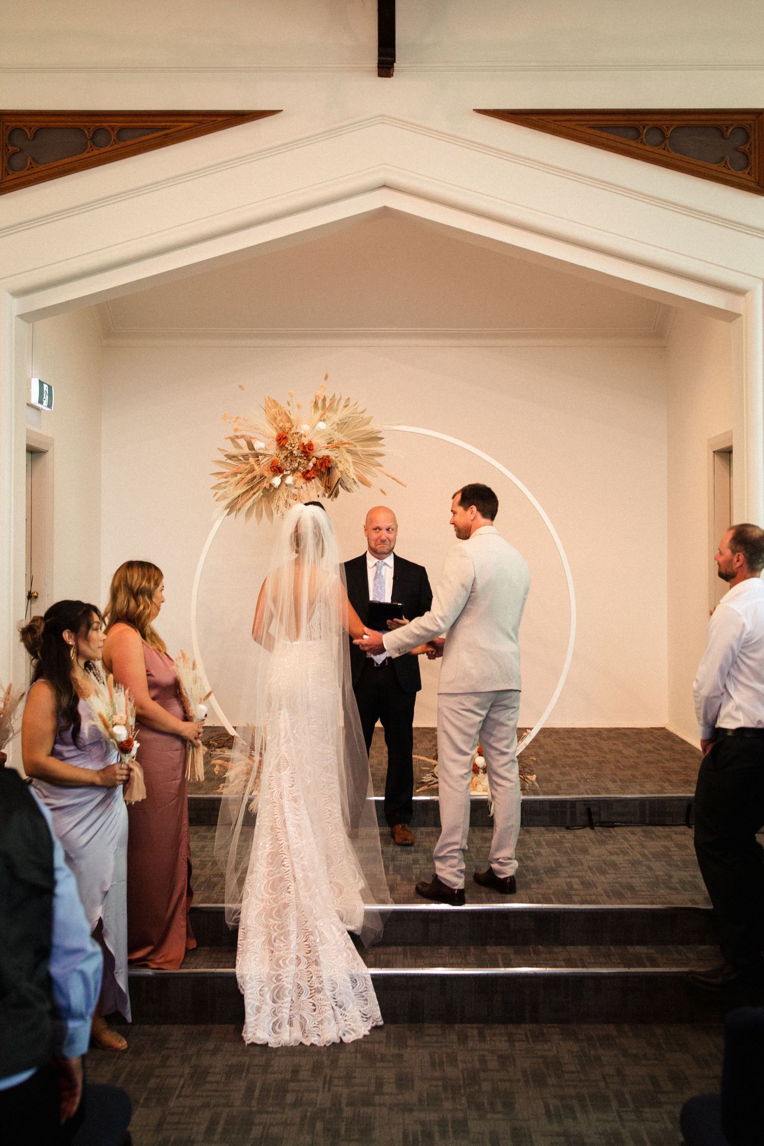 Wedding ceremony under an arch with dried floral arrangements in a church setting.