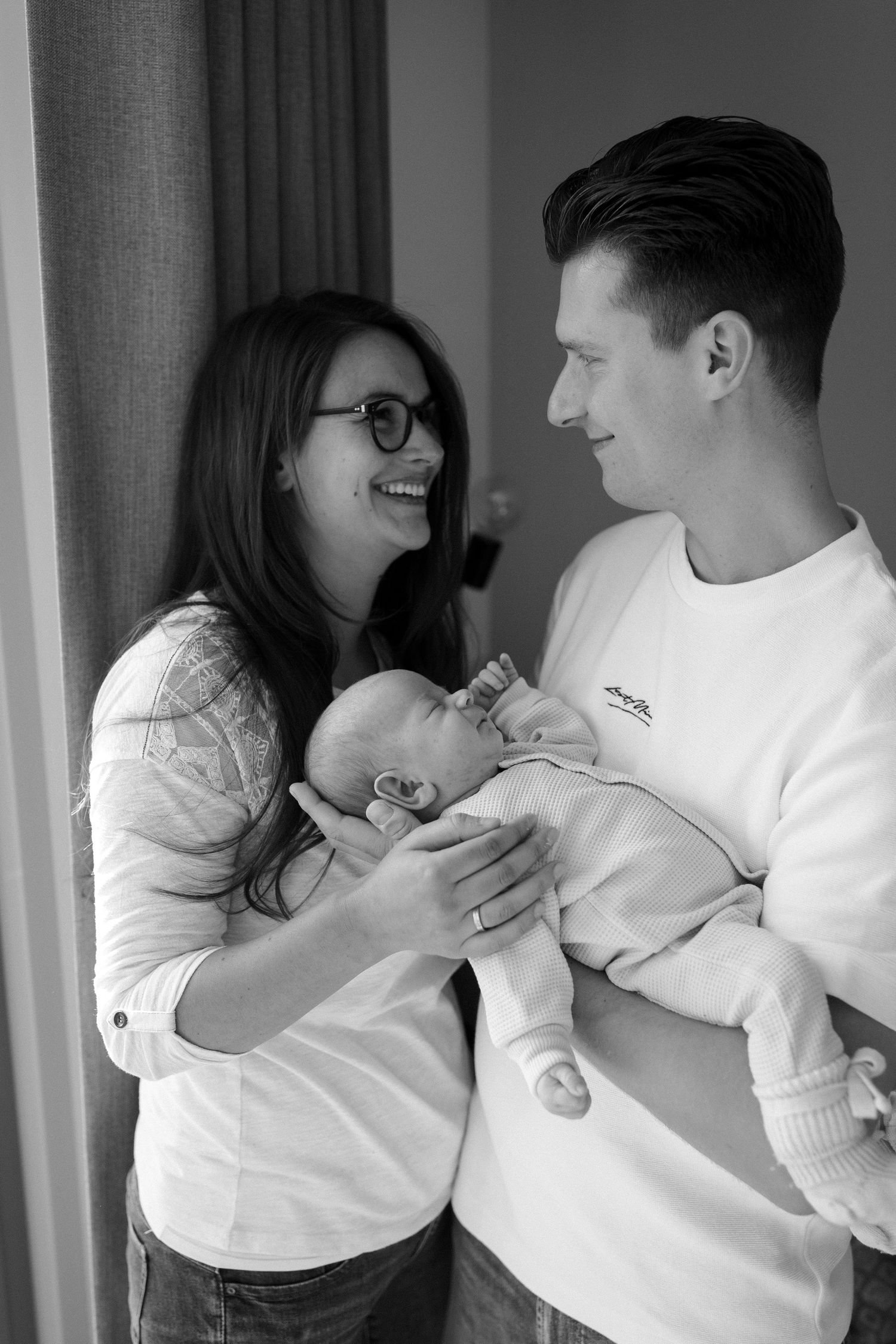 Black and white portrait of parents sharing intimate moment with newborn.