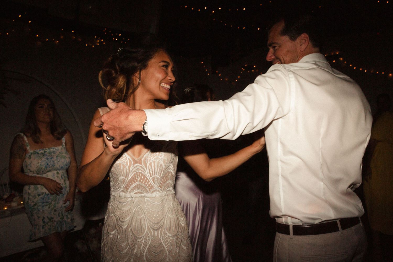 A couple shares a playful dance moment under atmospheric lighting at a reception.