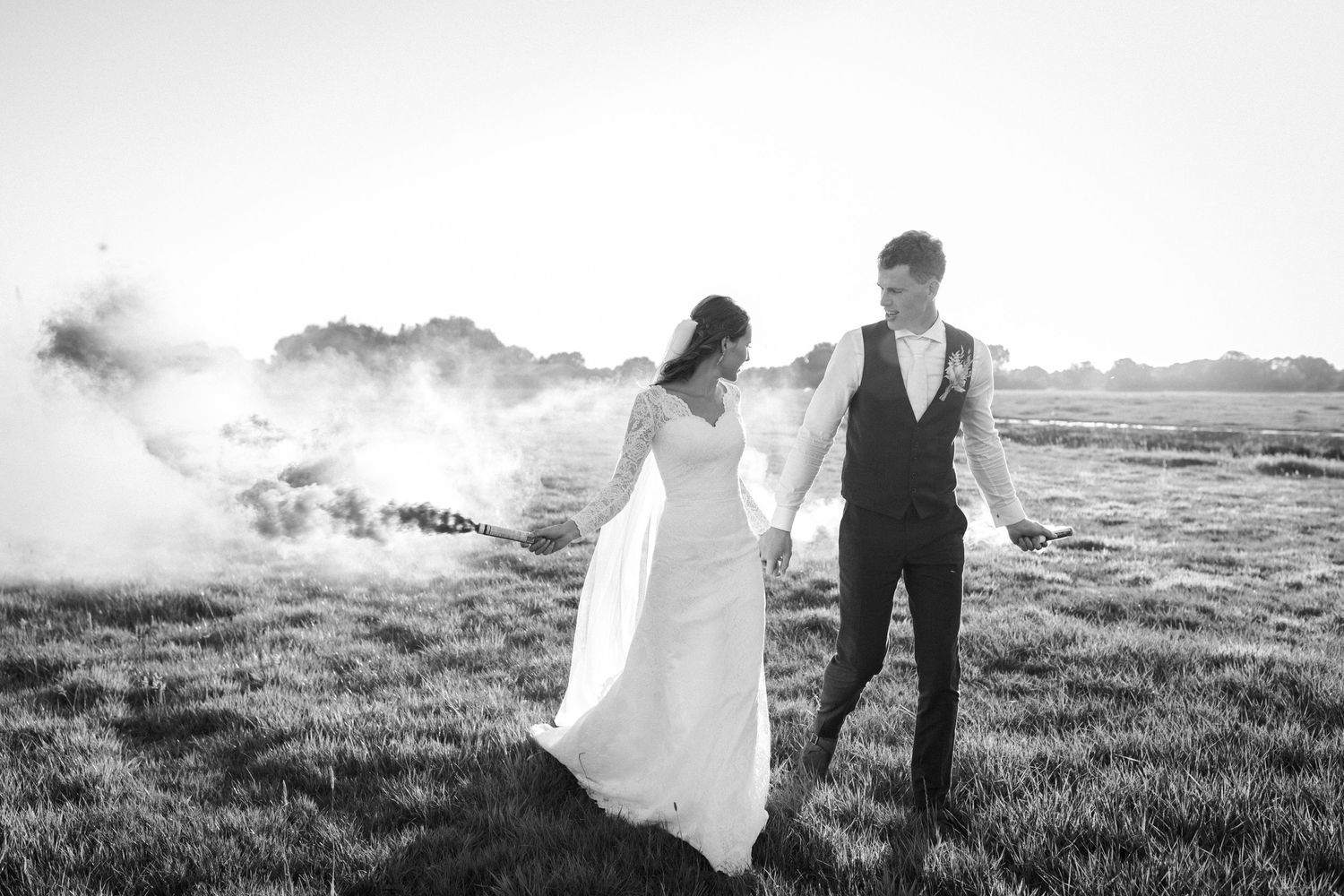 Bride and groom hold hands while walking through a misty field in black and white photograph.
