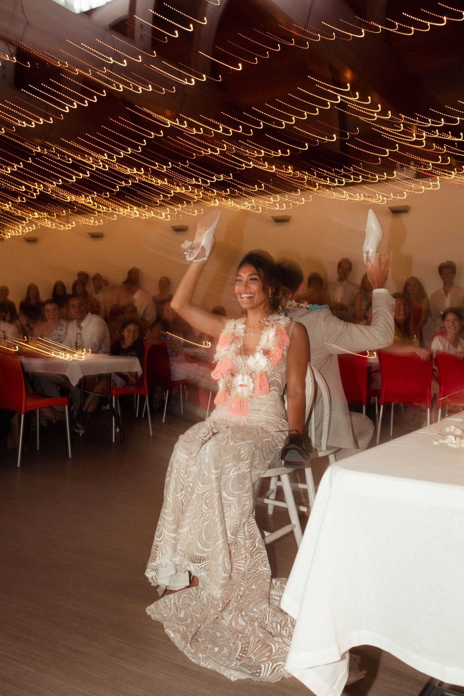 A person in a lace dress dances under warm glowing string lights at a reception venue.