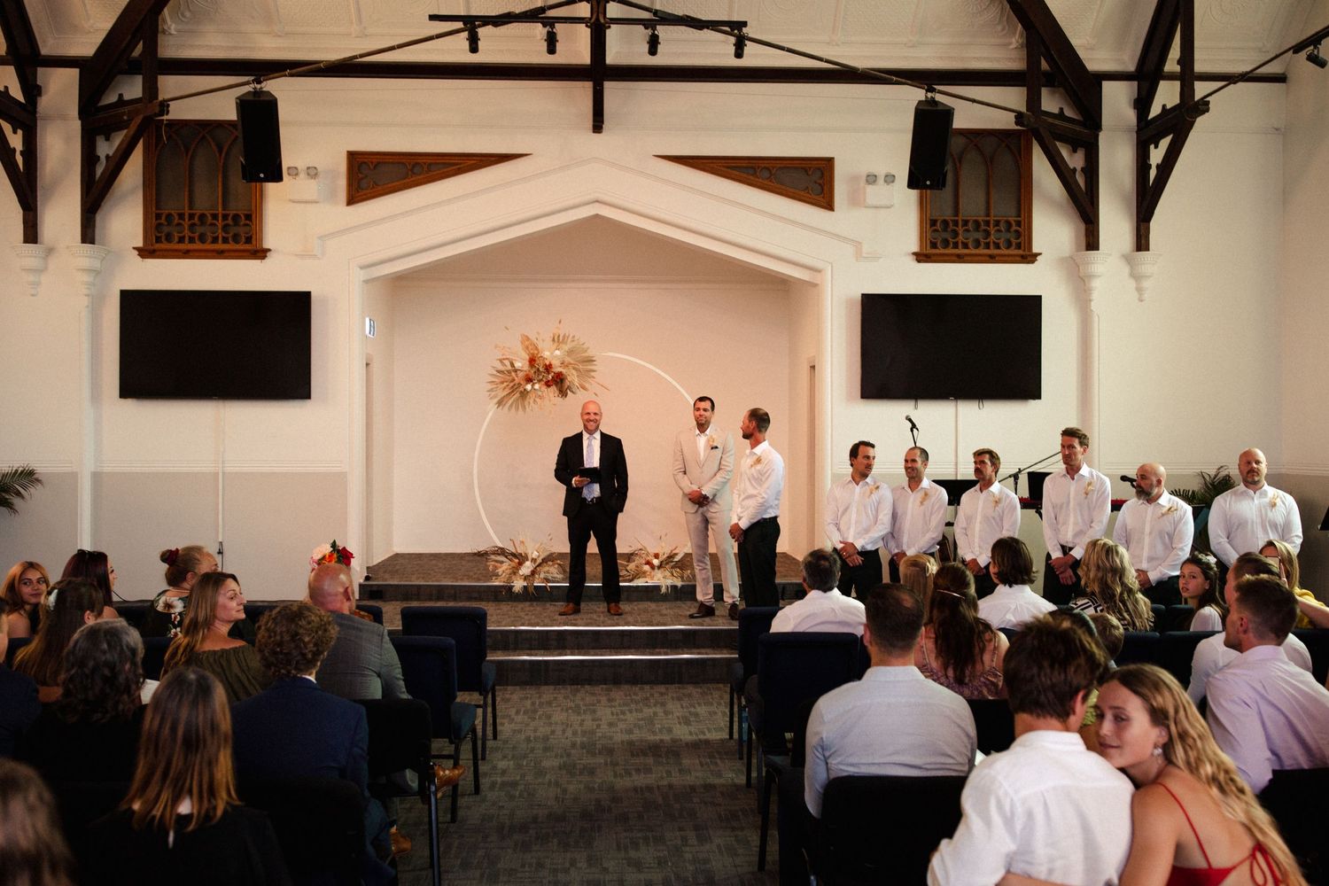 A wedding ceremony takes place in a classic church interior with wooden beams and white walls.