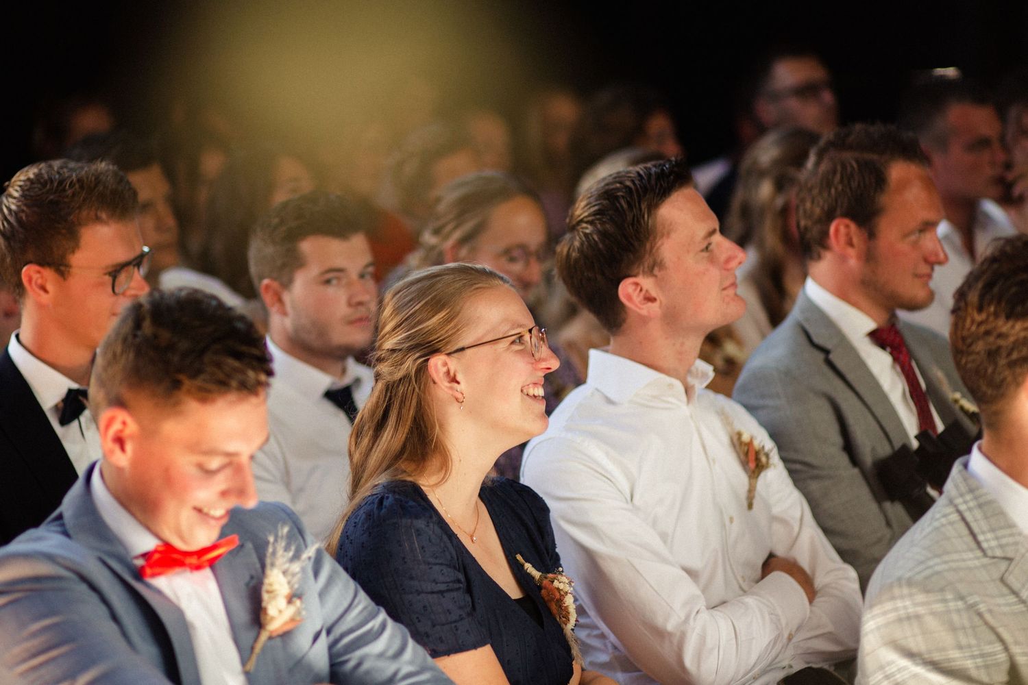 Audience members sitting in rows smile and laugh while watching a performance or presentation.
