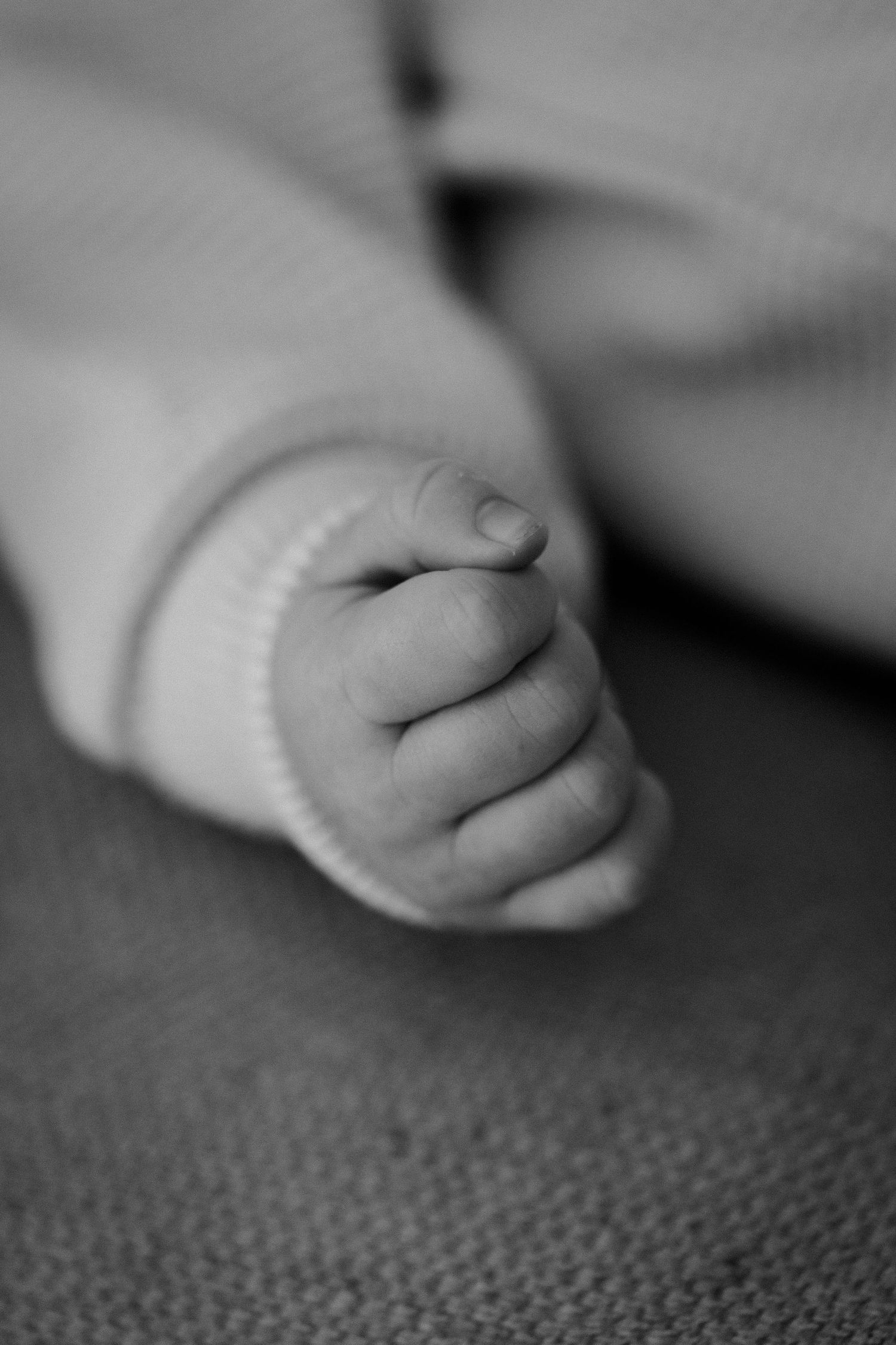 Close up black and white image of newborn's tiny fist against textured background.
