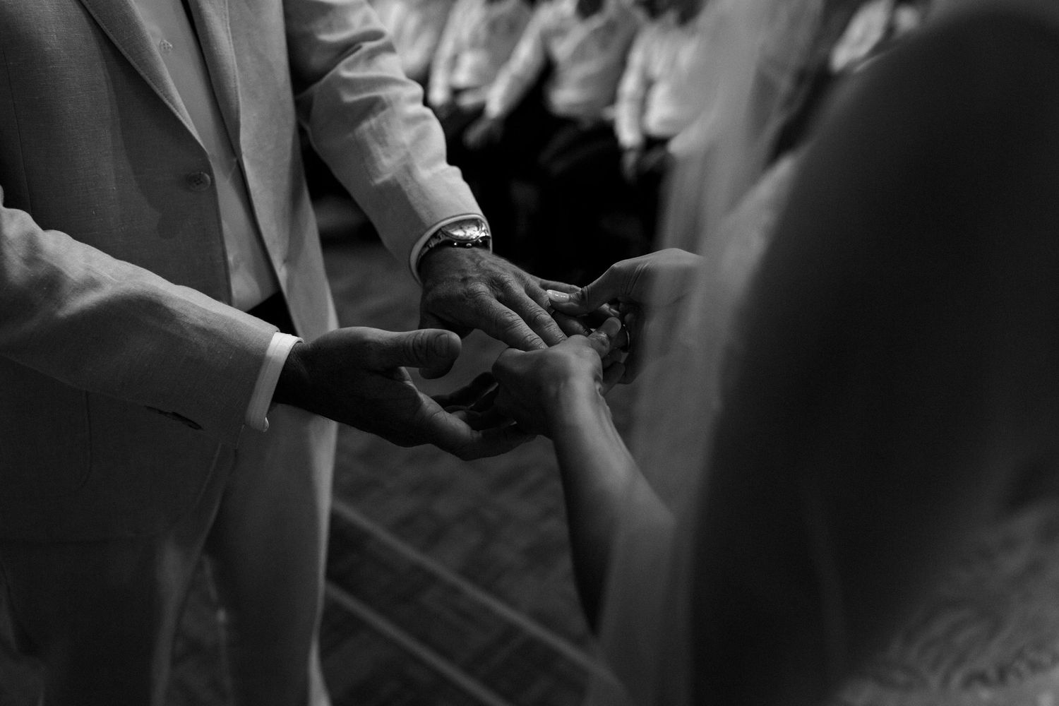 Black and white close-up of exchanging wedding rings during ceremony.
