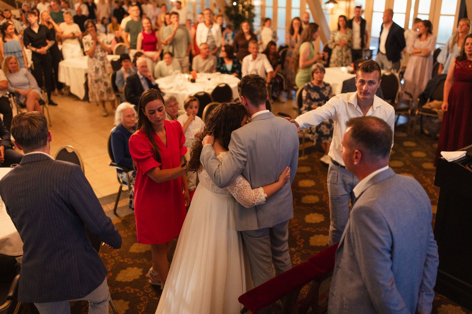 Wedding guests gather in an elegant reception hall with high ceilings and warm lighting.