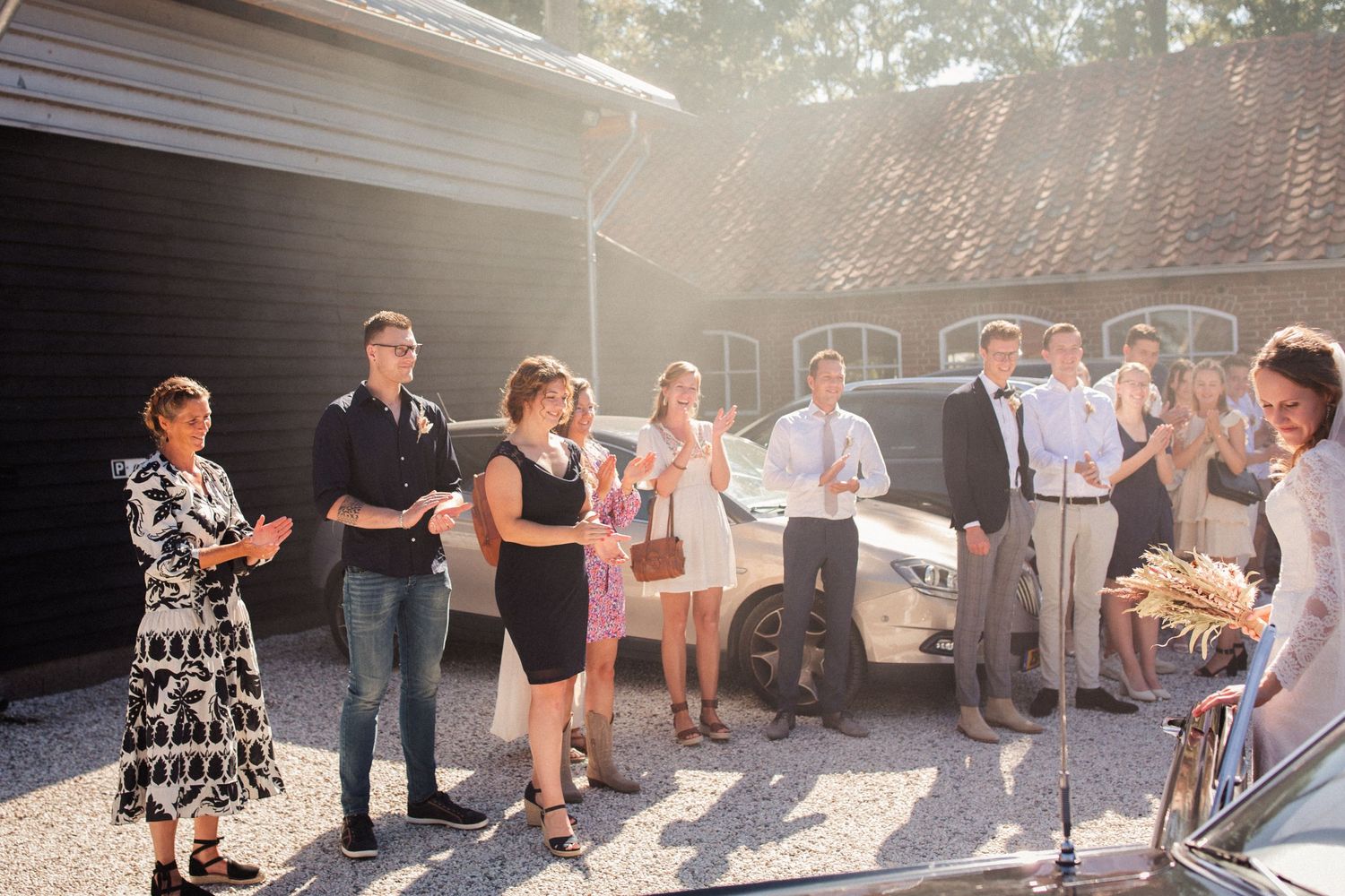 A group of wedding guests gather outdoors during a casual daytime celebration event.